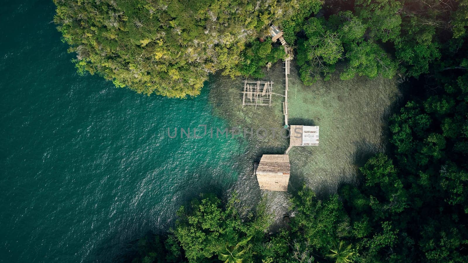 Drone, ocean and wood building in nature by beach, forest and woods with trees outdoor in Malaysia. Kelong, aerial view and house at sea for fishing, offshore or travel by water in summer environment.