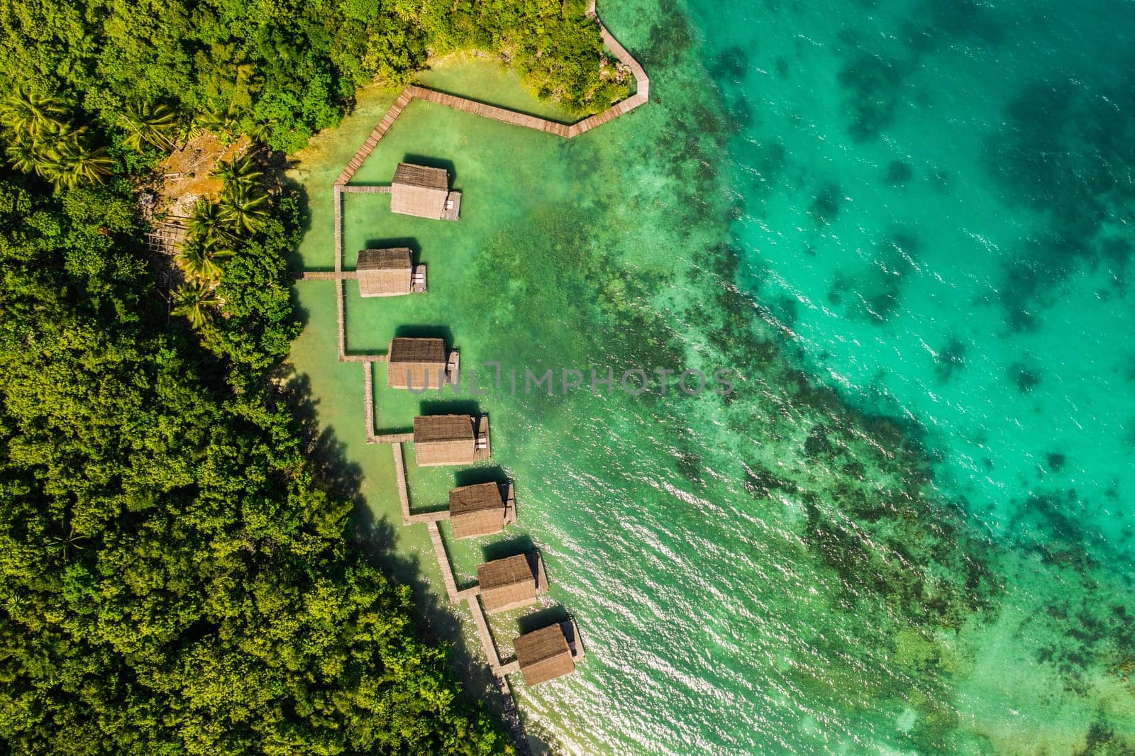 Aerial, buildings and lodge by tropical sea with bridge, island and trees on beach for tourism agency. Jetty, hotel and outdoor with ocean, hospitality and drone in nature with waves in Raja Ampat by YuriArcurs