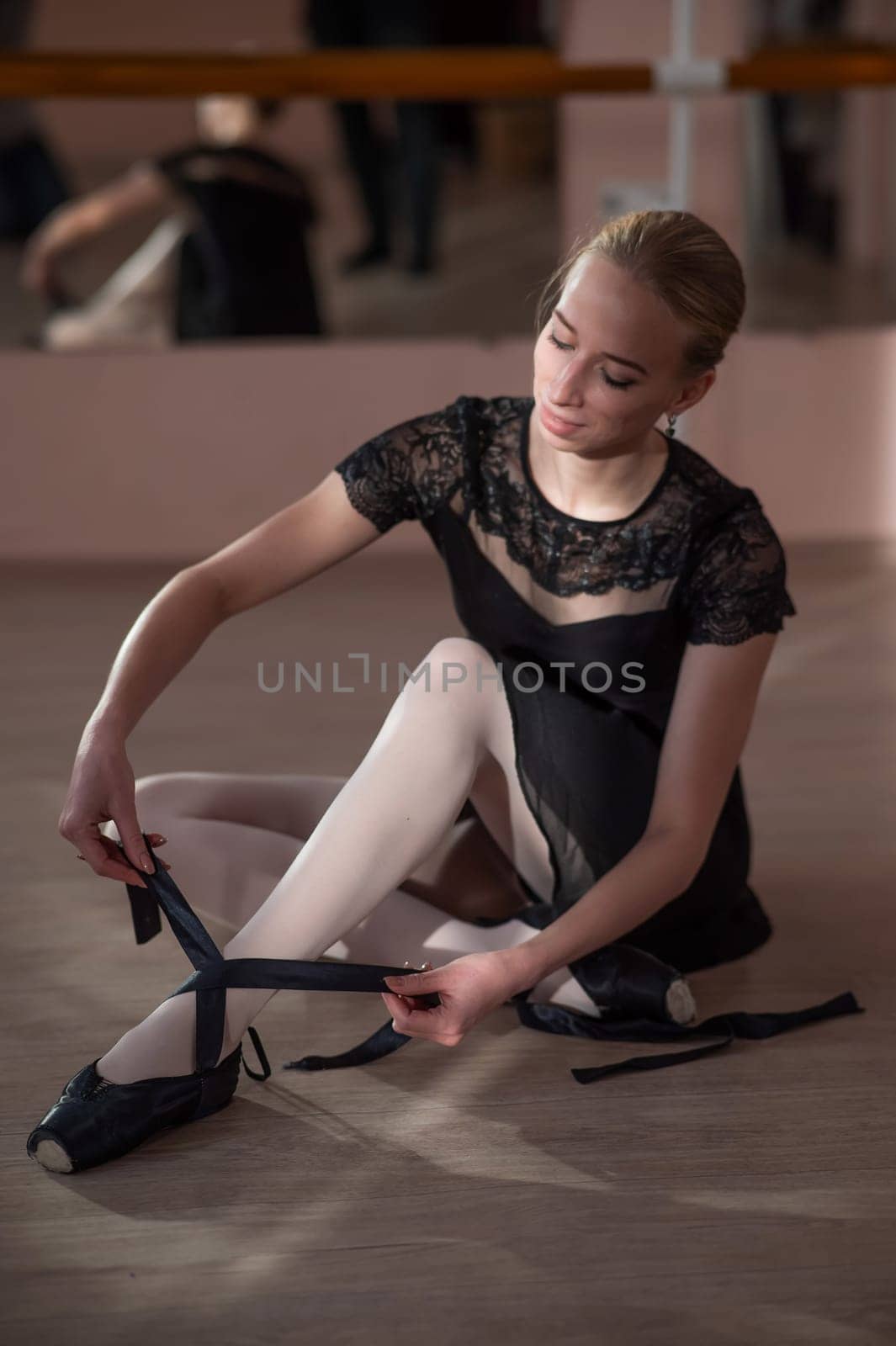 Woman sitting on the floor and tying ribbons on her pointe shoes. Vertical photo. by mrwed54