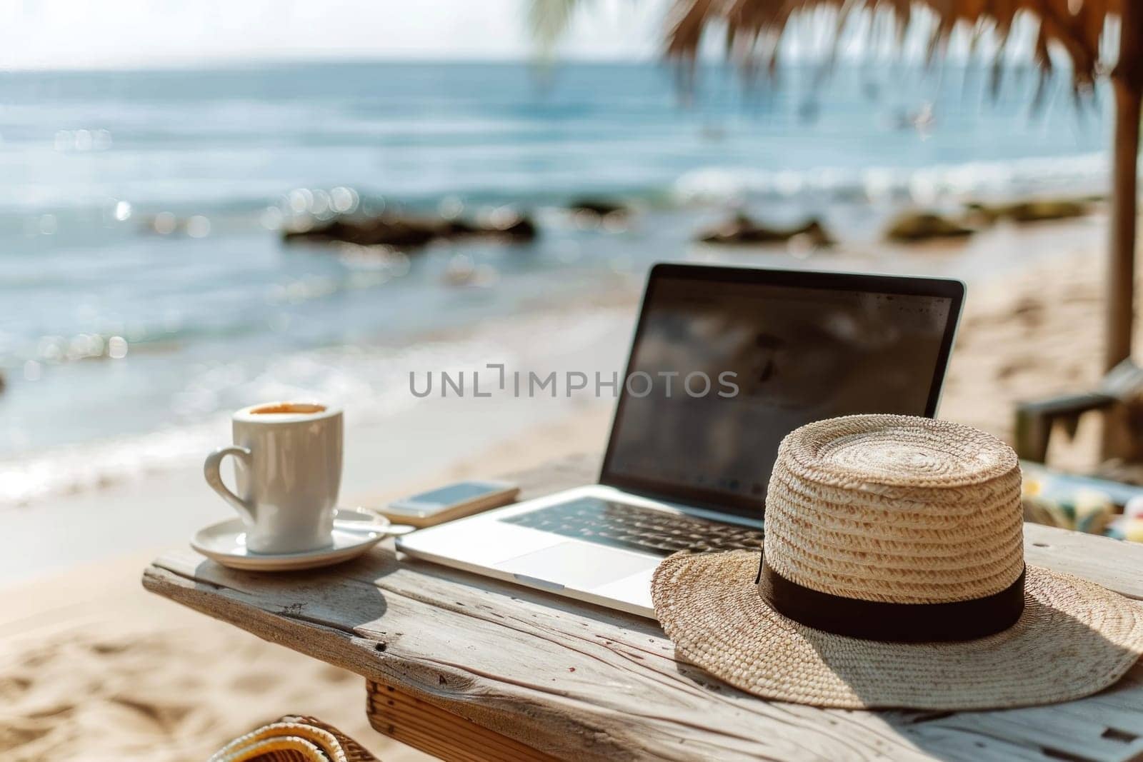 A laptop is open on a table next to a straw hat and a cup.