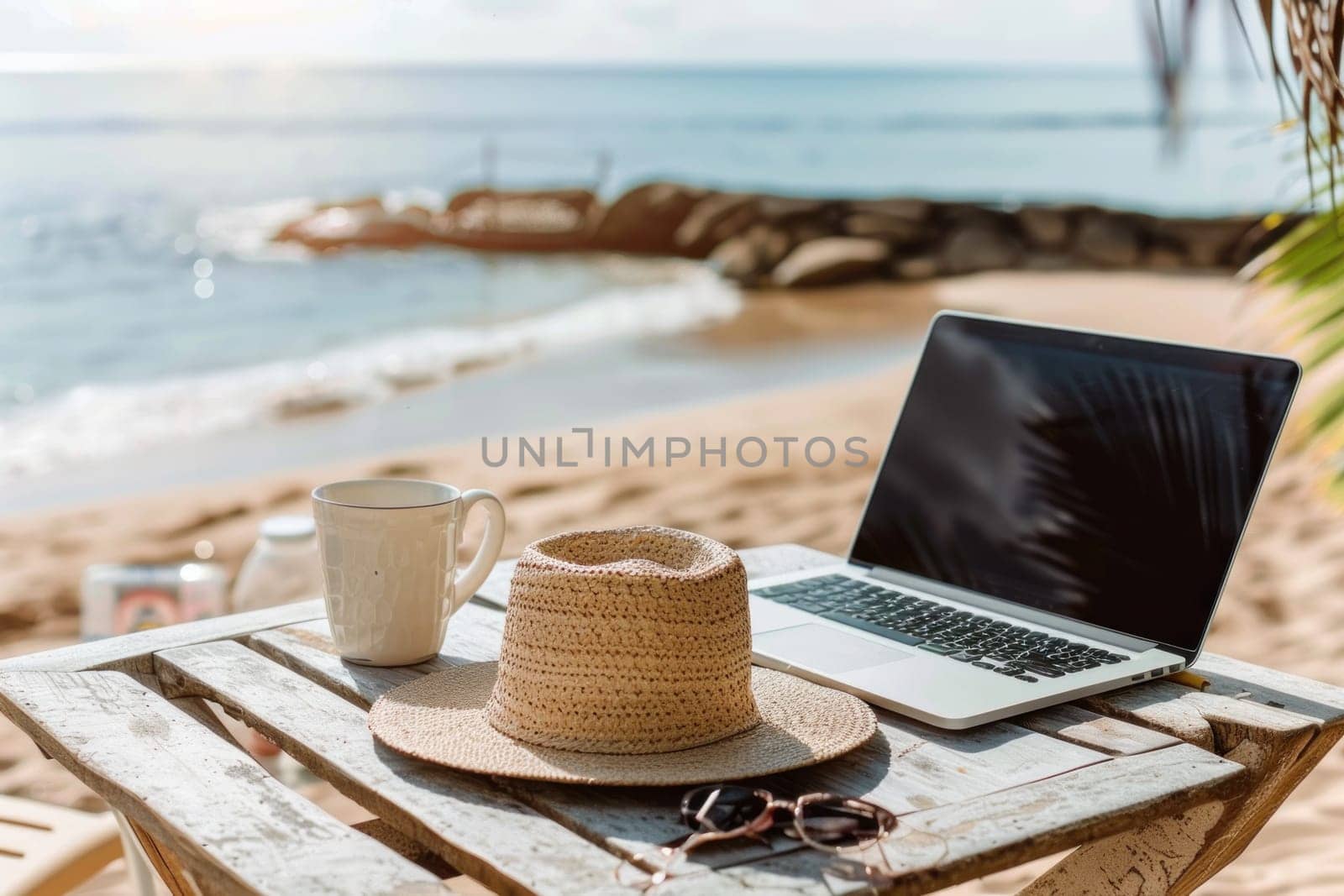A laptop is open on a table next to a straw hat and a cup.