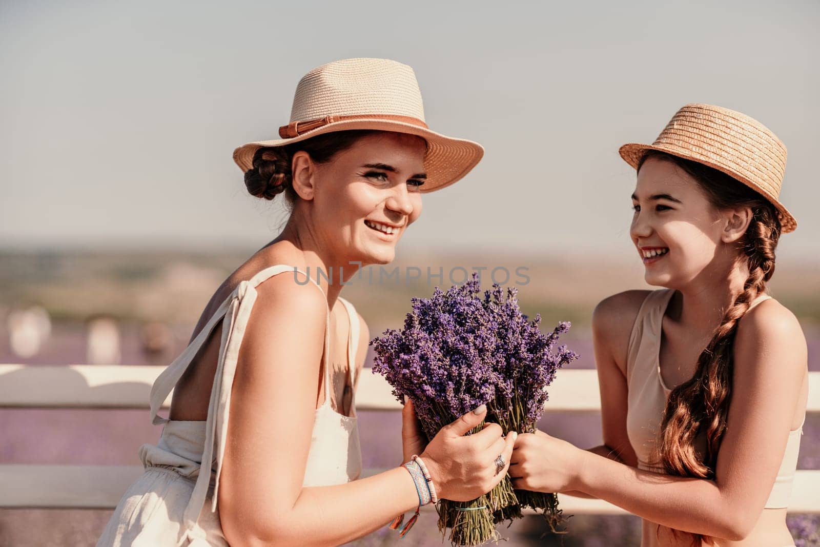 A woman and a child are sitting on a bench in a field of purple flowers lavande. The woman is holding a bouquet of flowers and the child is holding a bouquet of flowers as well.