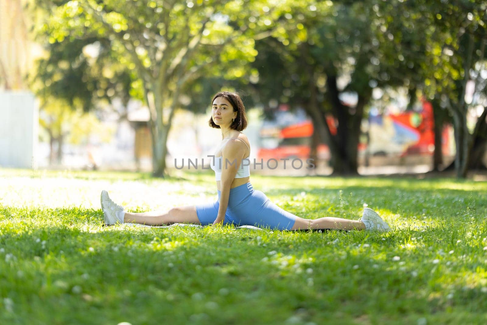 A woman is doing a split on a grassy field. Concept of freedom and relaxation, as the woman is stretching her body in a natural setting