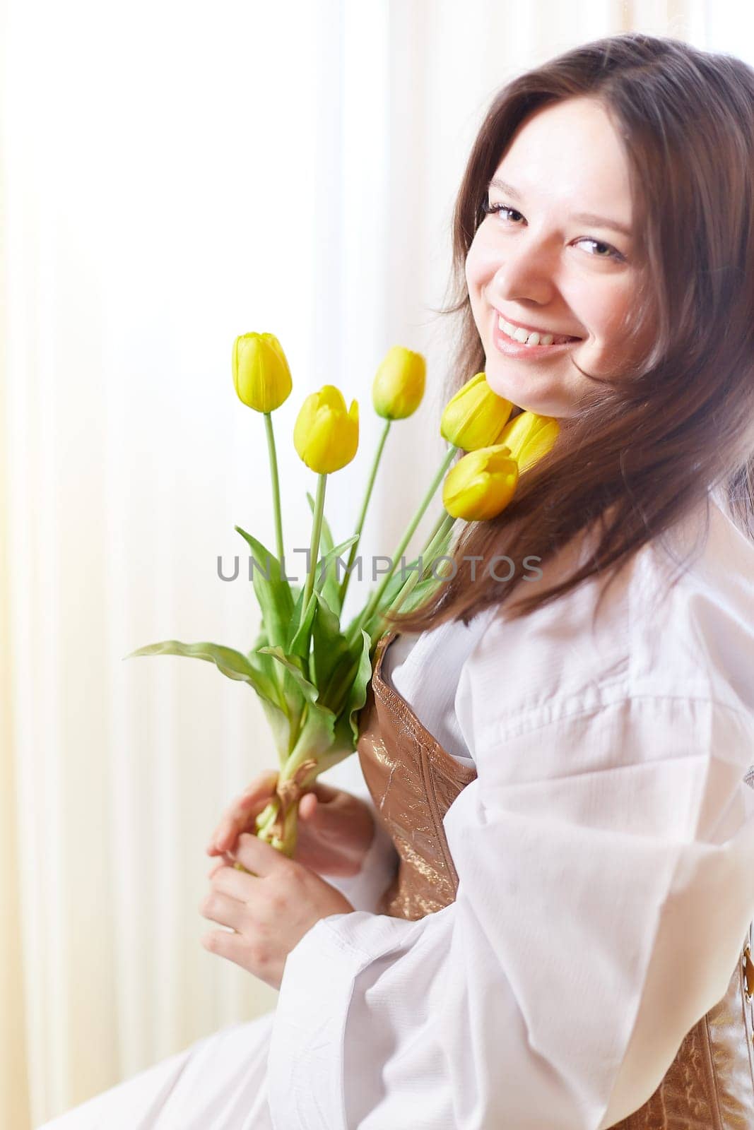 Beautiful sweet girl in nightgown in early morning with bouquet of delicate yellow tulips. Gift on International Women's Day on March 8th. Cosmetics, skin and hair care. Perfume, natural fragrance