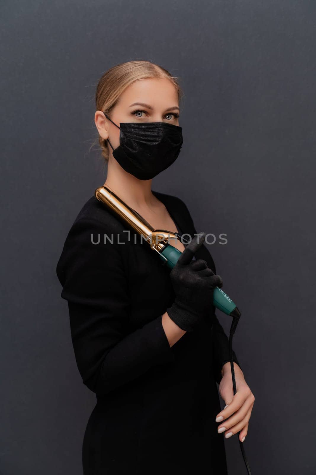 A woman in a black dress holding a hair curler. She is wearing a mask. Concept of caution and responsibility in the face of a pandemic