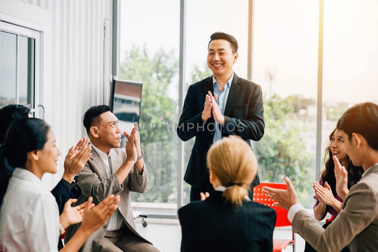 In a meeting, a male speaker shares expertise with the diverse audience. Participants actively raise their hands, asking questions and exemplifying teamwork, learning, and support. by Sorapop