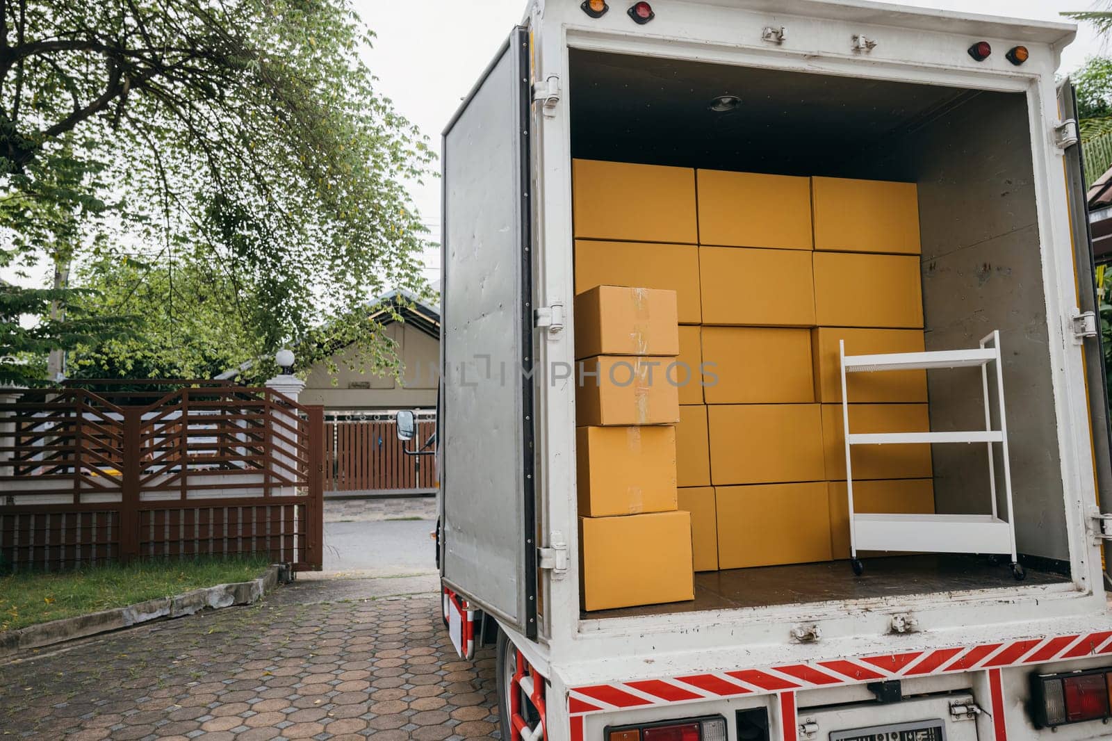 Logistic service outdoors, Open car trunk carrying moving cardboard boxes. White delivery van for house relocation. Transporting items scene. Moving Day Concept. by Sorapop