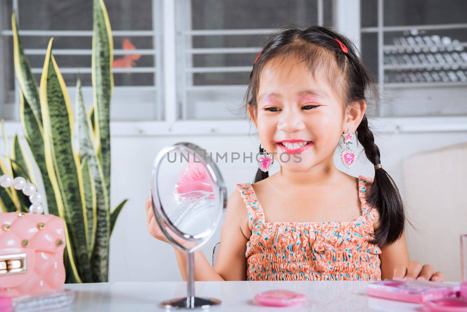 little girl making makeup her face she look in the mirror and applying red lipstick to mouth by Sorapop
