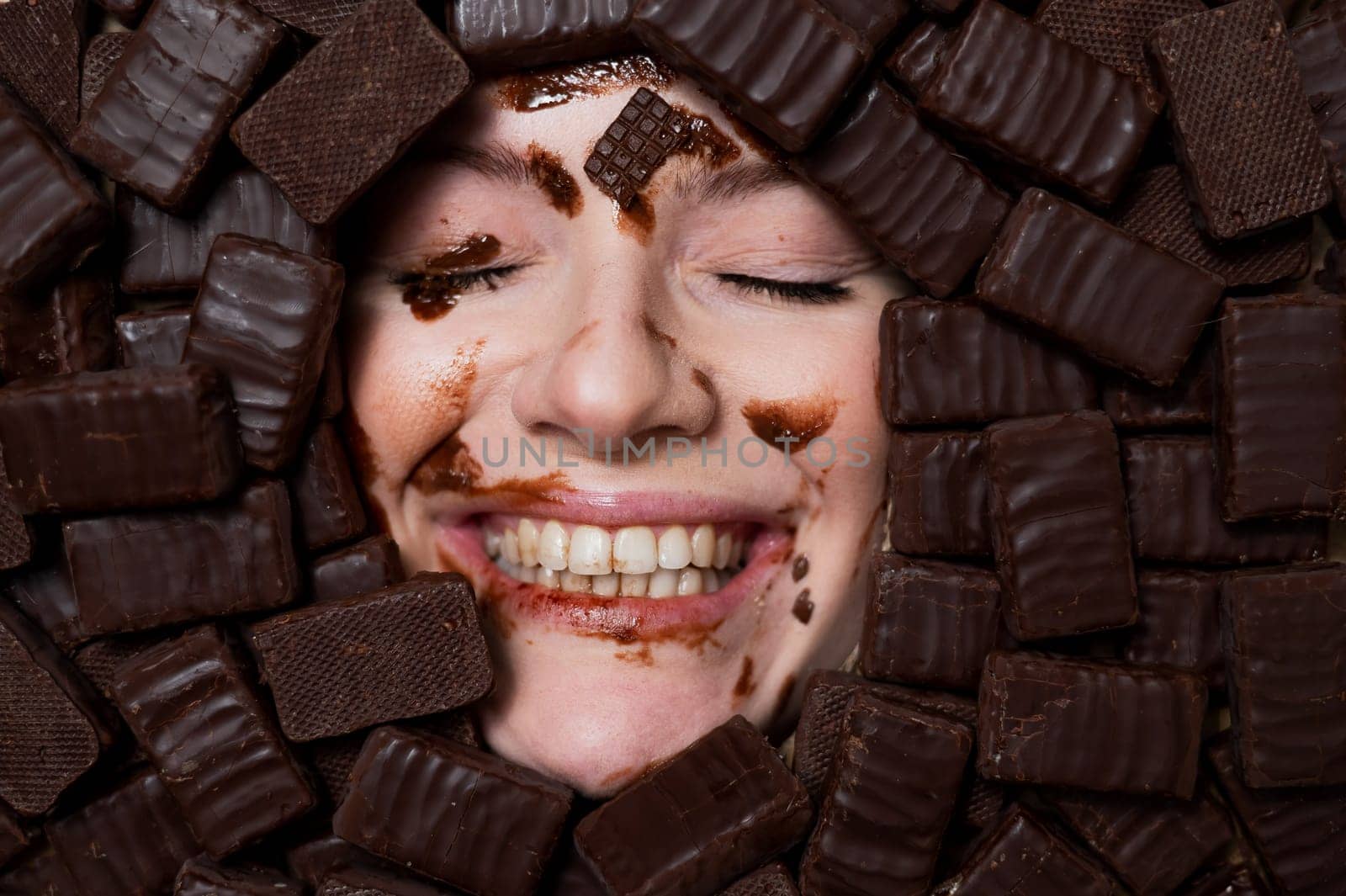 The face of a caucasian woman surrounded by sweets. The girl is smeared in chocolate