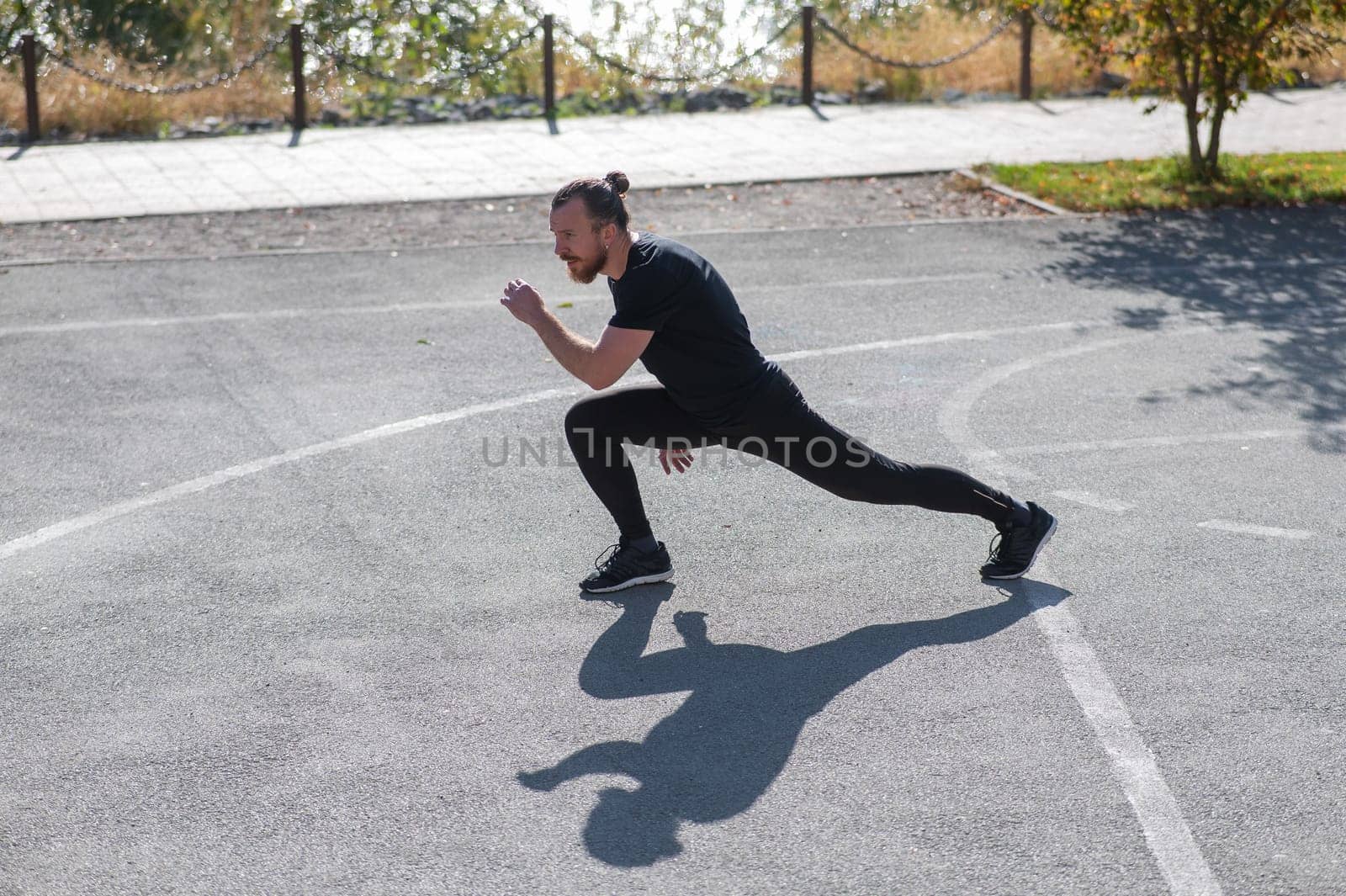 Bearded man with long hair doing lunges on the sports field