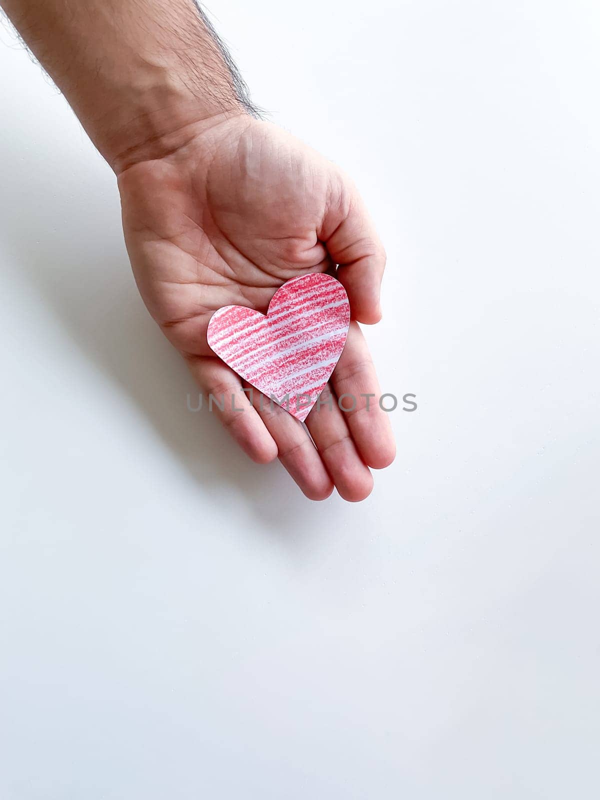 A mans hand holds a red paper heart on a white background. Empty space for an inscription. The concept of manifestation of love. High quality photo