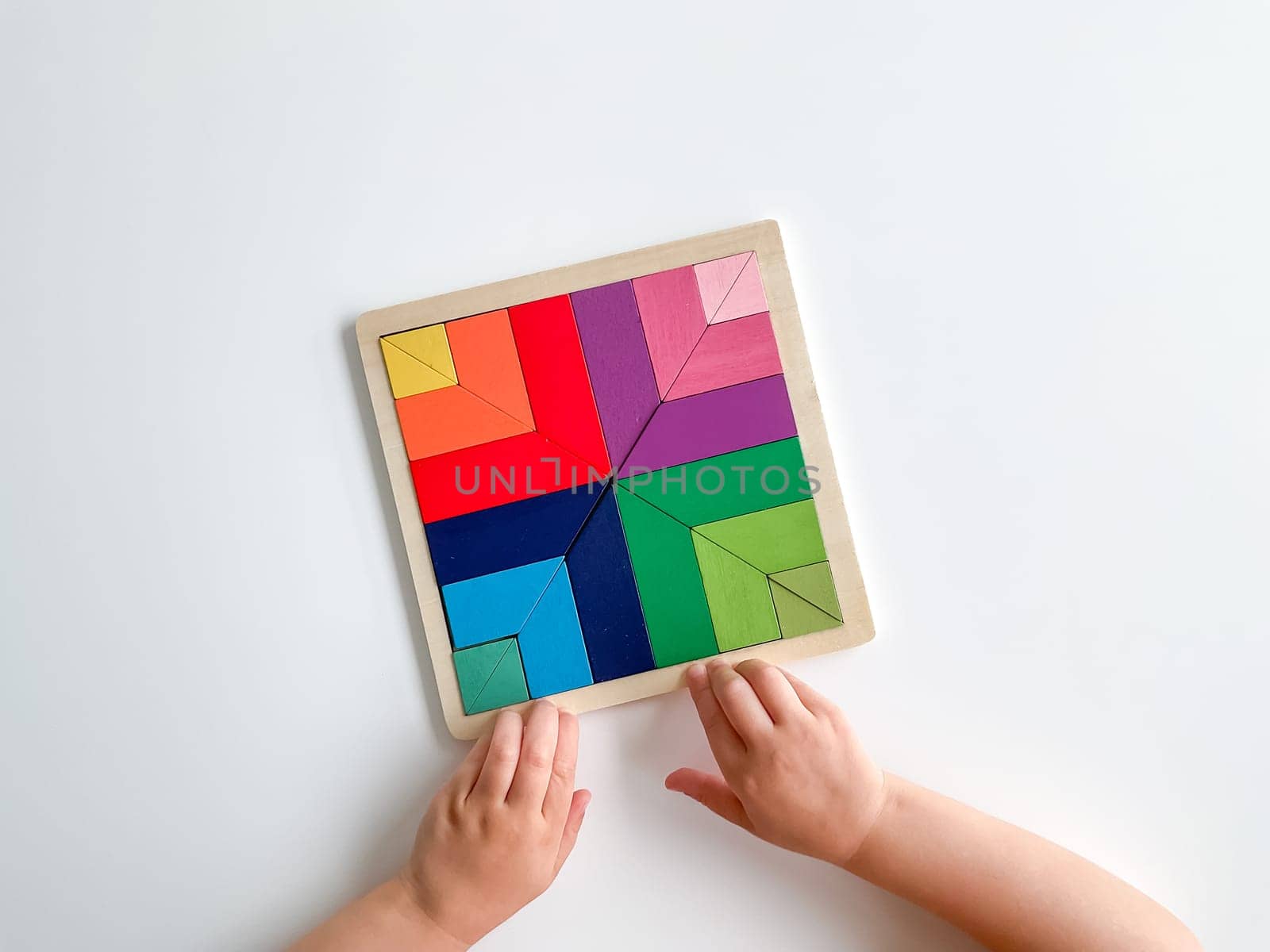 childs hand collects multicolored wooden mosaic on white background. by Lunnica