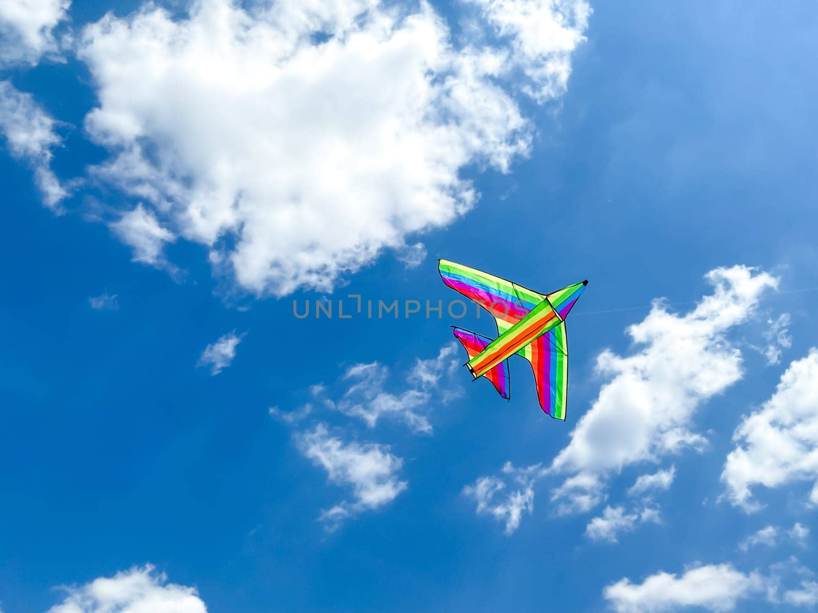 Multicolored kite flies in the blue sky on a sunny day. Empty space for an inscription. Multicolored kite in the form of an airplane. by Lunnica