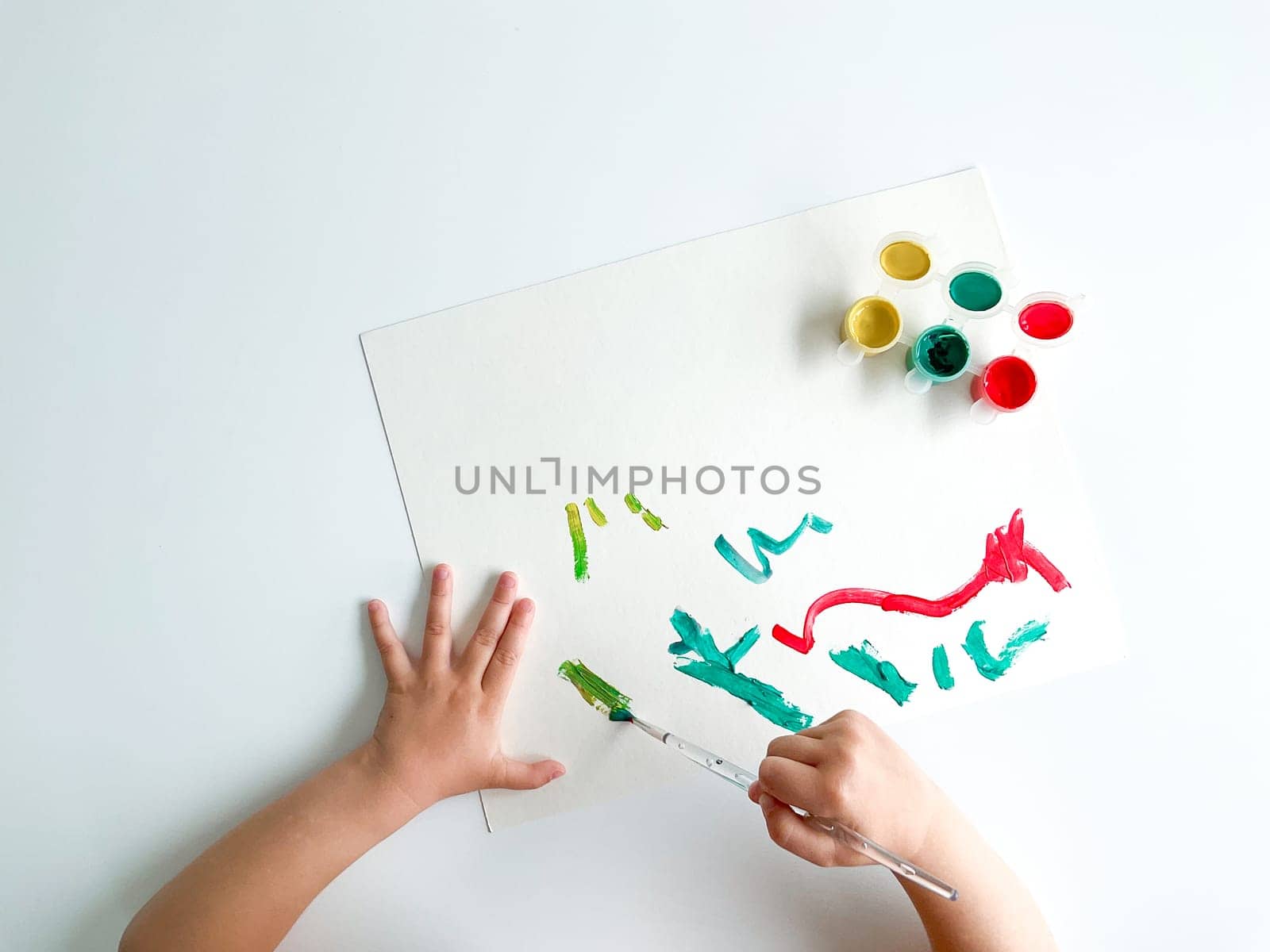 small child draws with paints and brush on white table. High quality photo