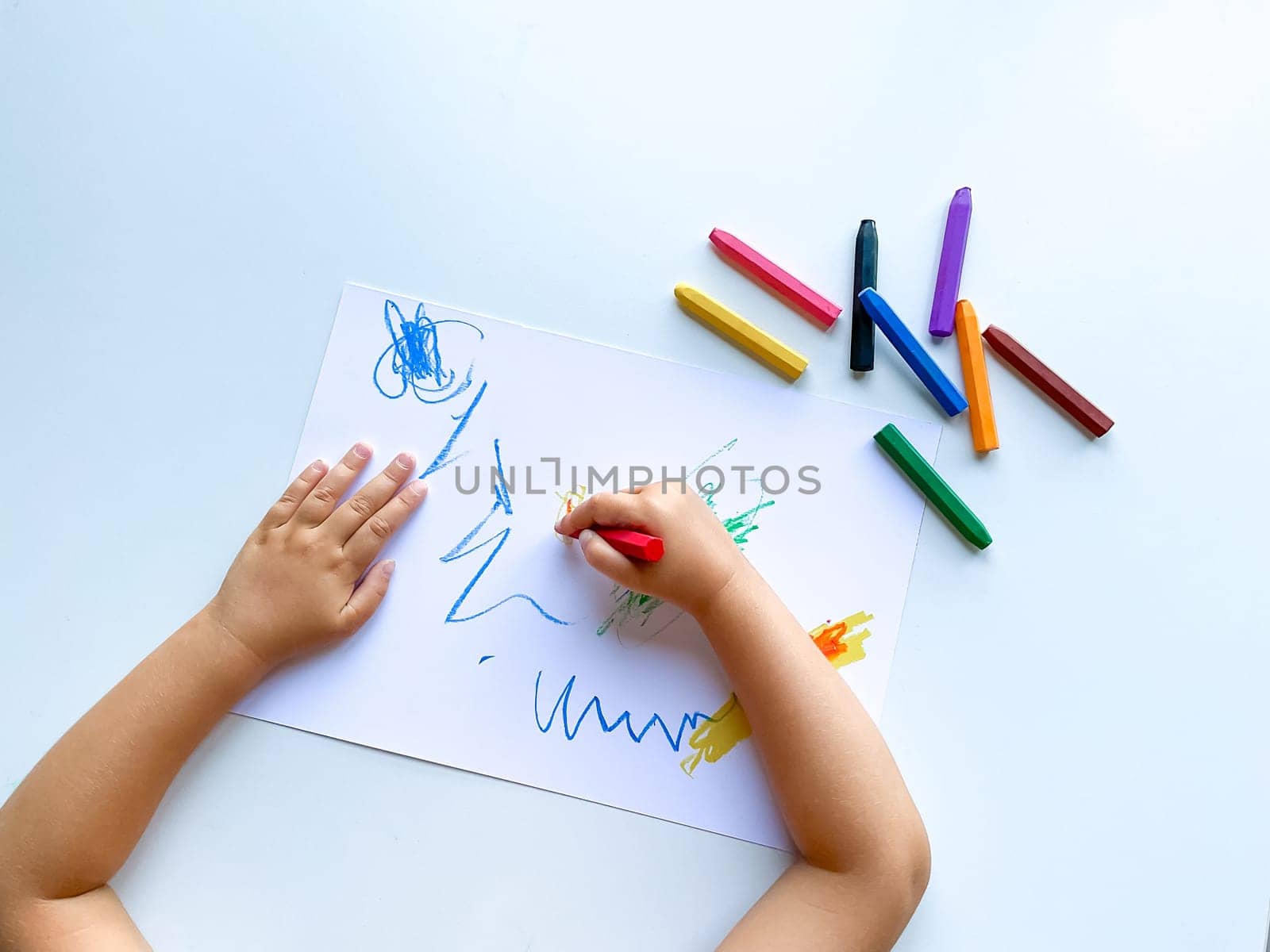 small child draws with pastel crayons on white table. High quality photo