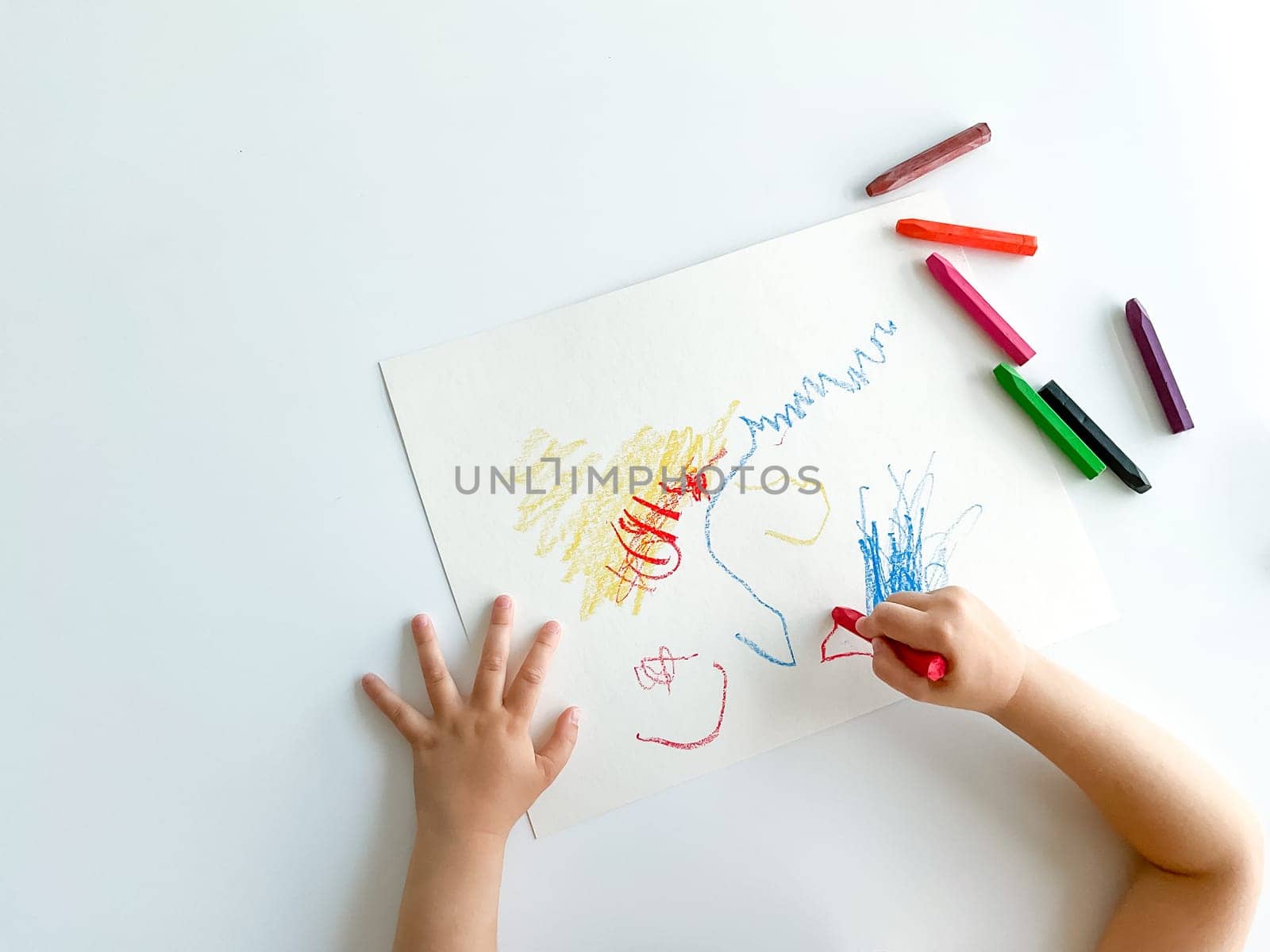 small child draws with pastel crayons on white table. by Lunnica