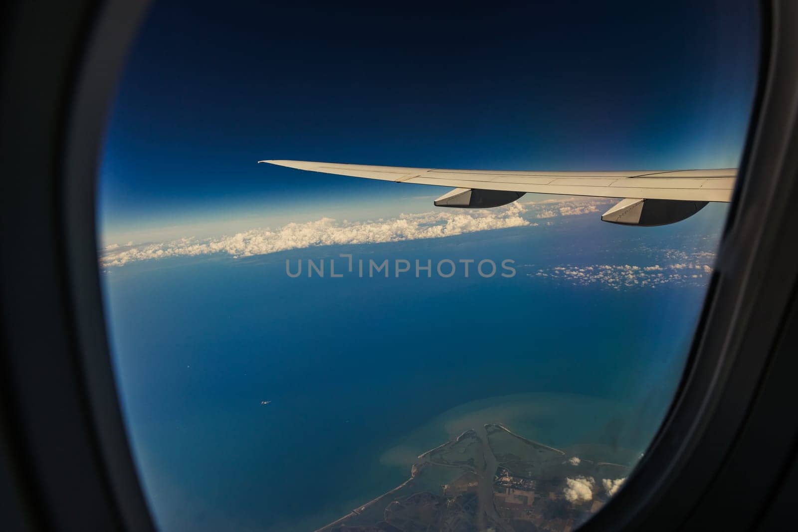 A beautiful view of the wing of an airplane, the sky, the sea and a piece of land through the airplane window in the evening summer, close-up side view.