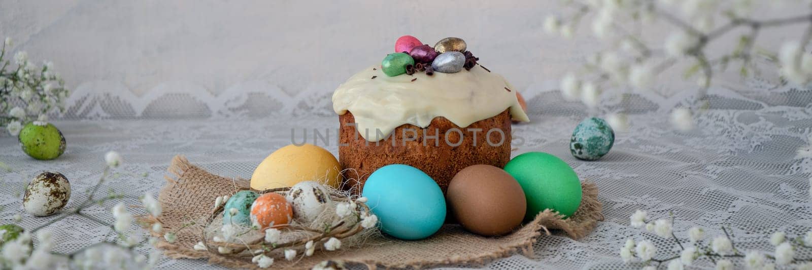 banner of Easter cake decorated with chocolate eggs, colored eggs on a lace white tablecloth. Happy Easter concept. white spring flowers. soft focus. copy space,