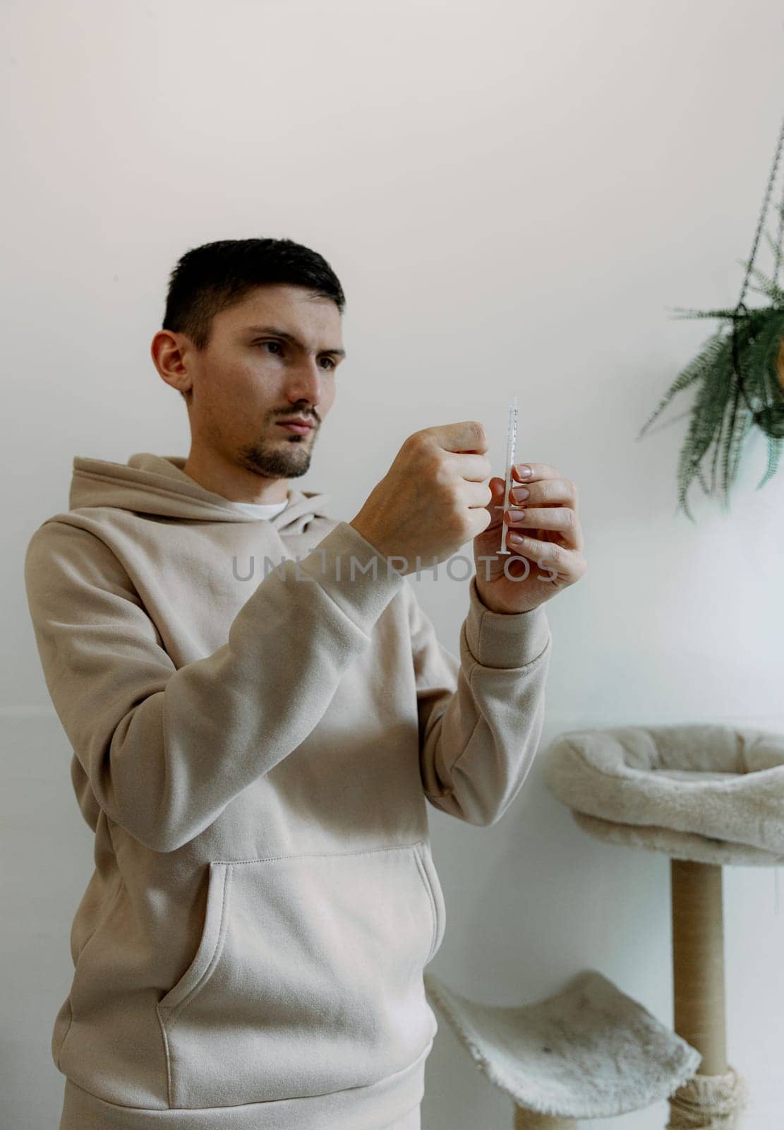 One young Caucasian handsome brunette man with a serious emotion takes medicine from a bottle with a syringe to treat his cat at home, standing in the kitchen, close-up side view.