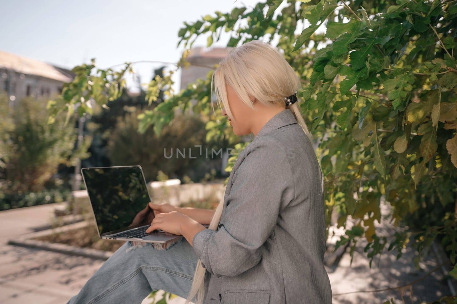 A woman is sitting on a bench with a laptop open in front of her. She is smiling and she is enjoying her time. Concept of relaxation and leisure