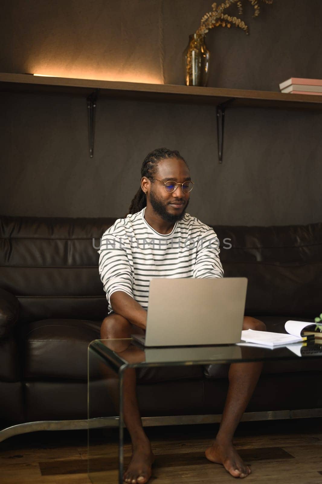 Portrait of young African American man sitting on couch working with laptop at home.
