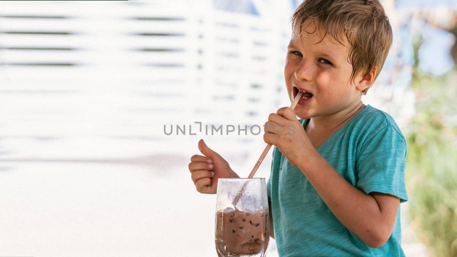 Happy childhood. Boy drinking chocolate tea with ice in hot summer day time. Cute lover of sweets and tasty things. Shows thumbs up by nandrey85