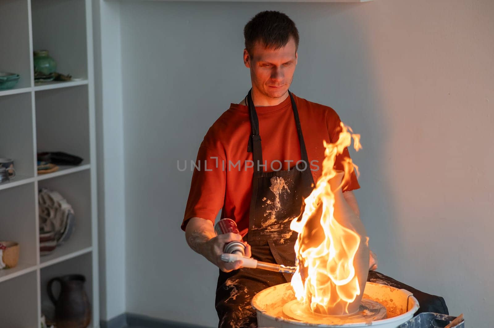 A potter burns a jug with a gas burner on a potter's wheel