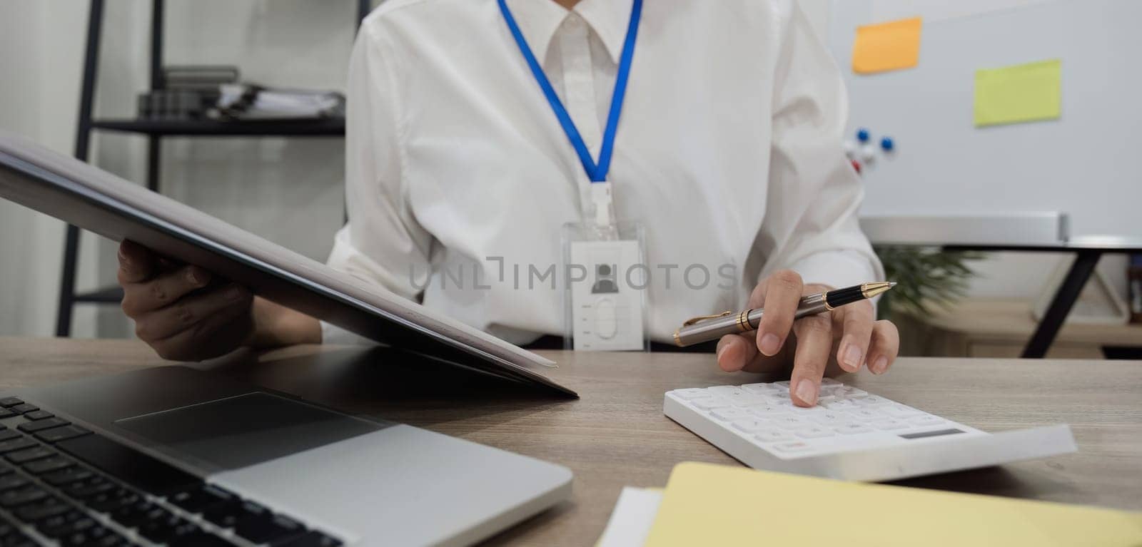 Asian female accountant Use a calculator to calculate business numbers on a white wooden table in the office. by wichayada