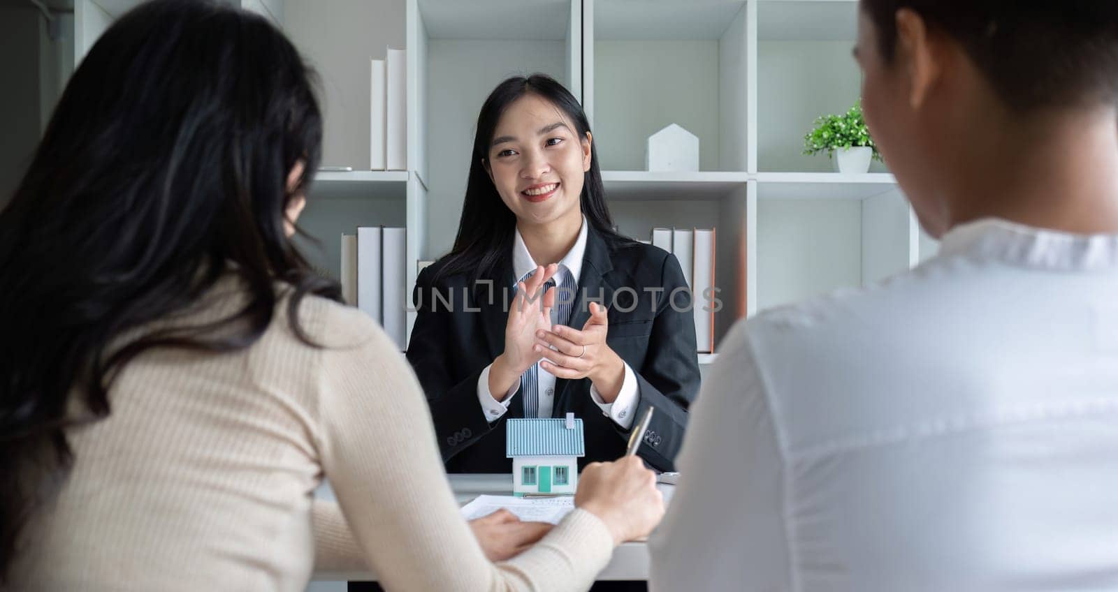 A real estate agent or insurance agent presents a house plan and insurance contract to an Asian couple..