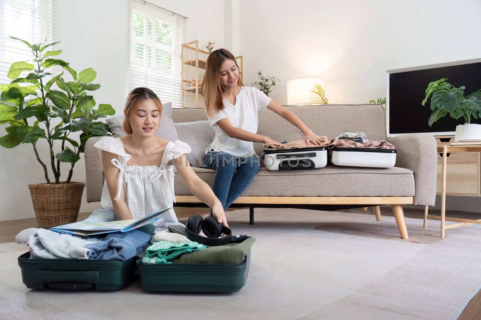 Young Asian woman packing clothes to the suitcase. Preparation for the summertime vacation. Two women are planning a trip and helping to prepare luggage to travel.