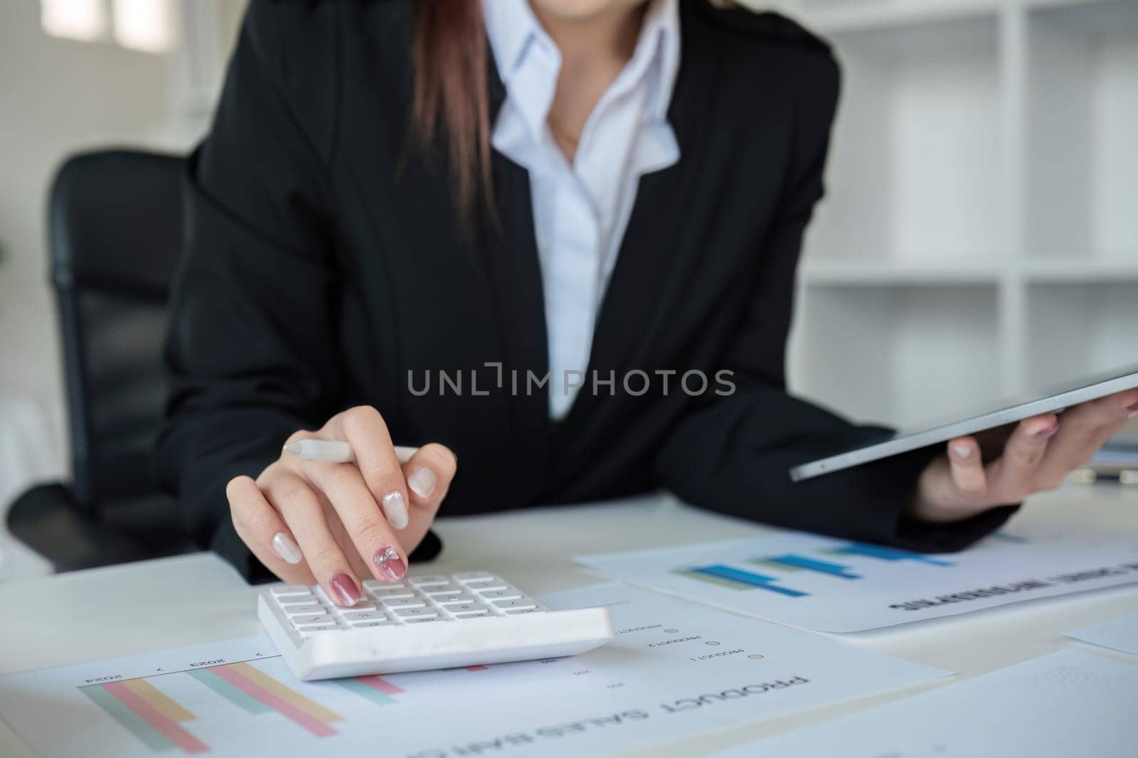 Young woman accountant uses calculator to calculate finances or graph business numbers on white wooden table in office..