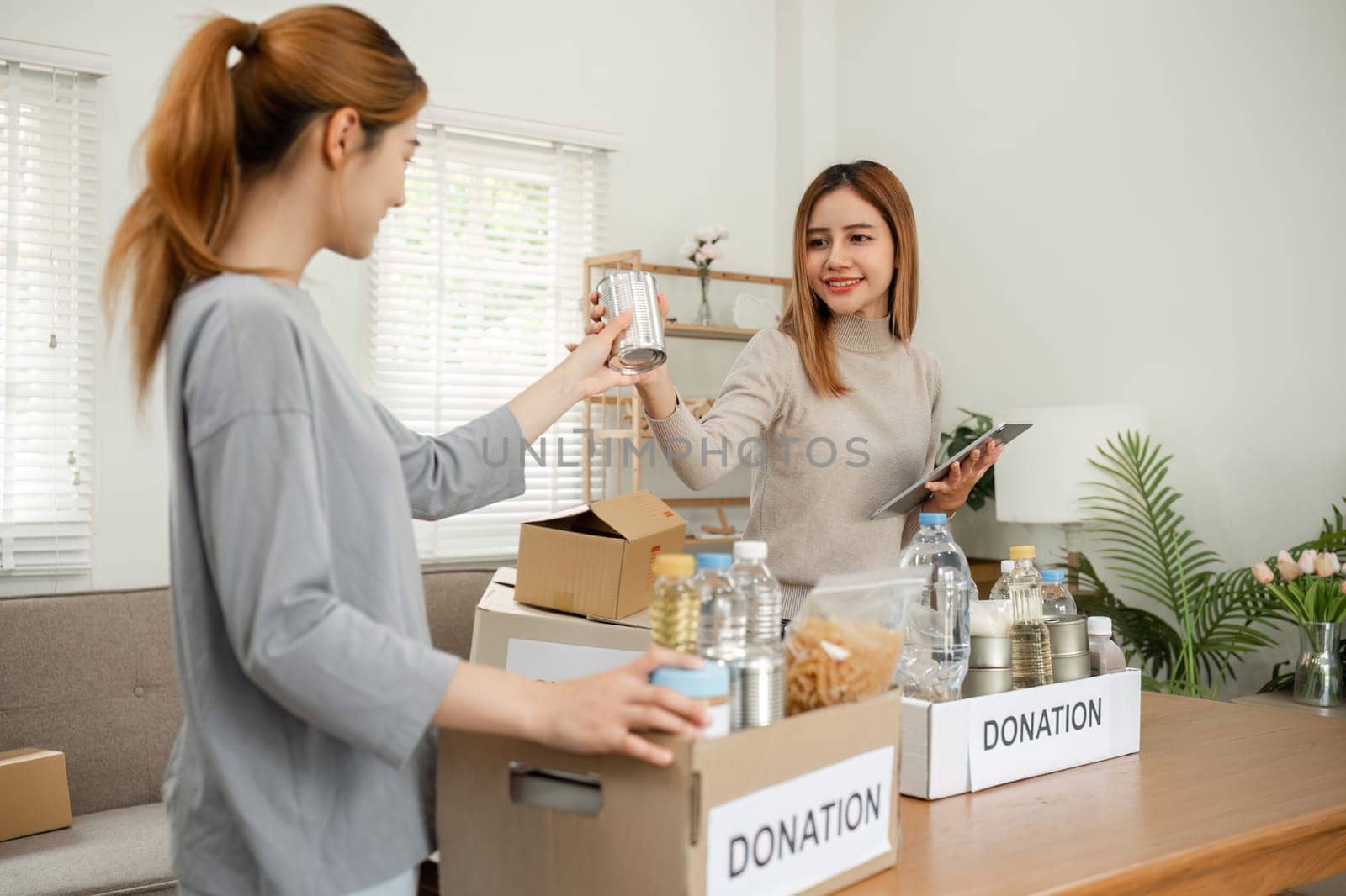 Two young female volunteers help pack food into donation boxes and prepare to donate them to charity. by wichayada