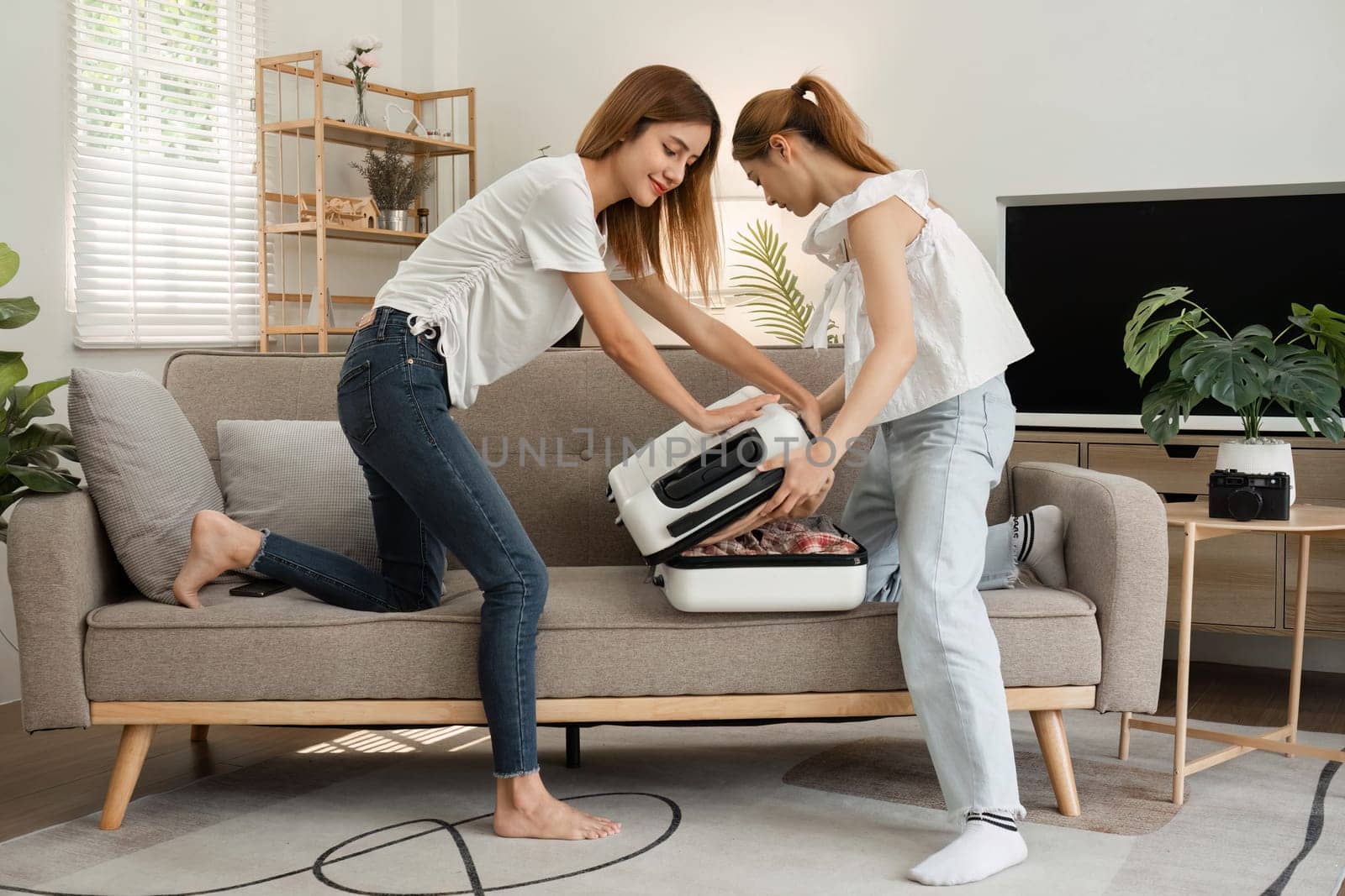 Two young female friends pack a suitcase with clothes and travel passports in preparation for a weekend away. by wichayada