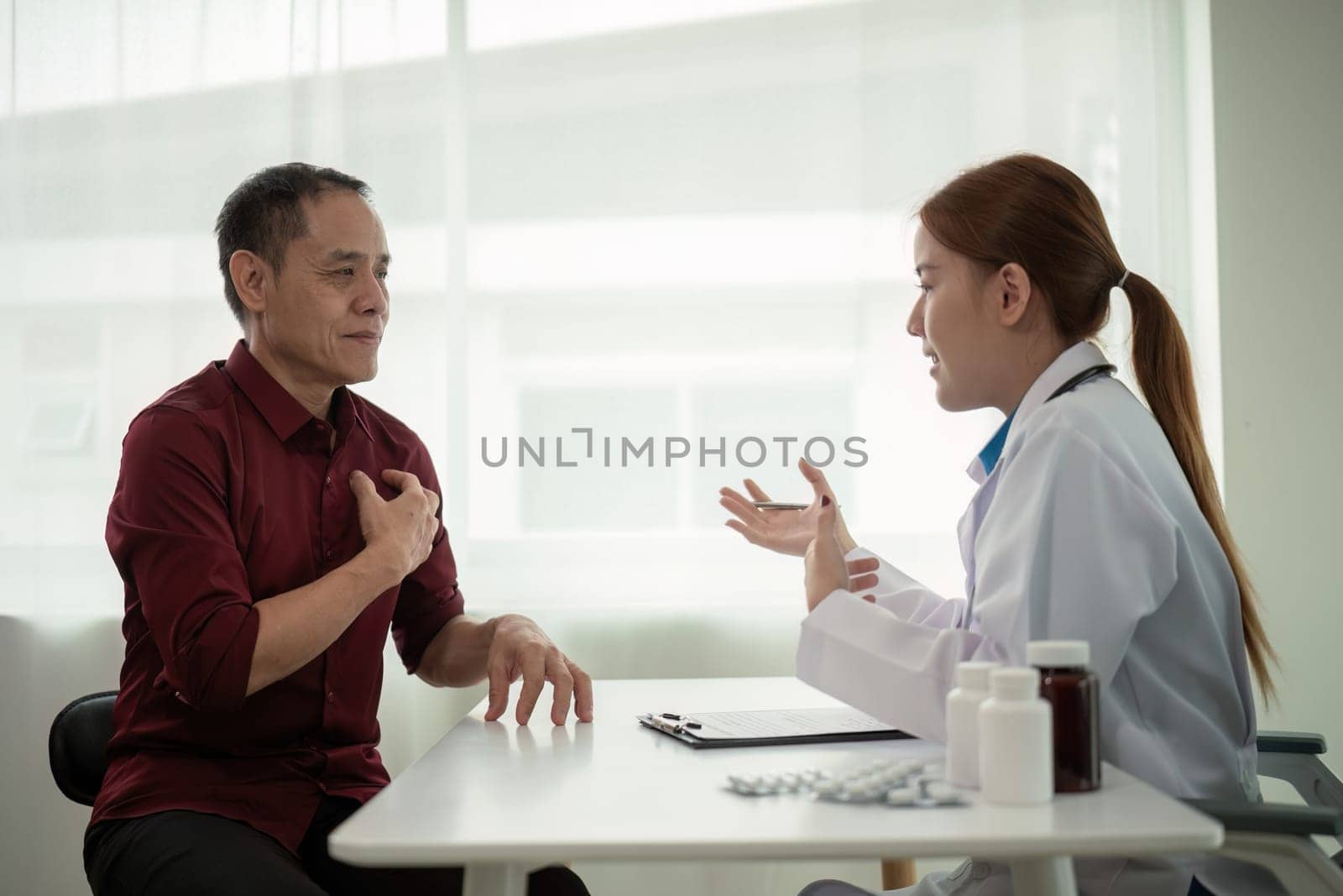 Doctor young woman white coat giving medical consultation to male elderly mature patient, discussing healthcare treatment or health test results at hospital.