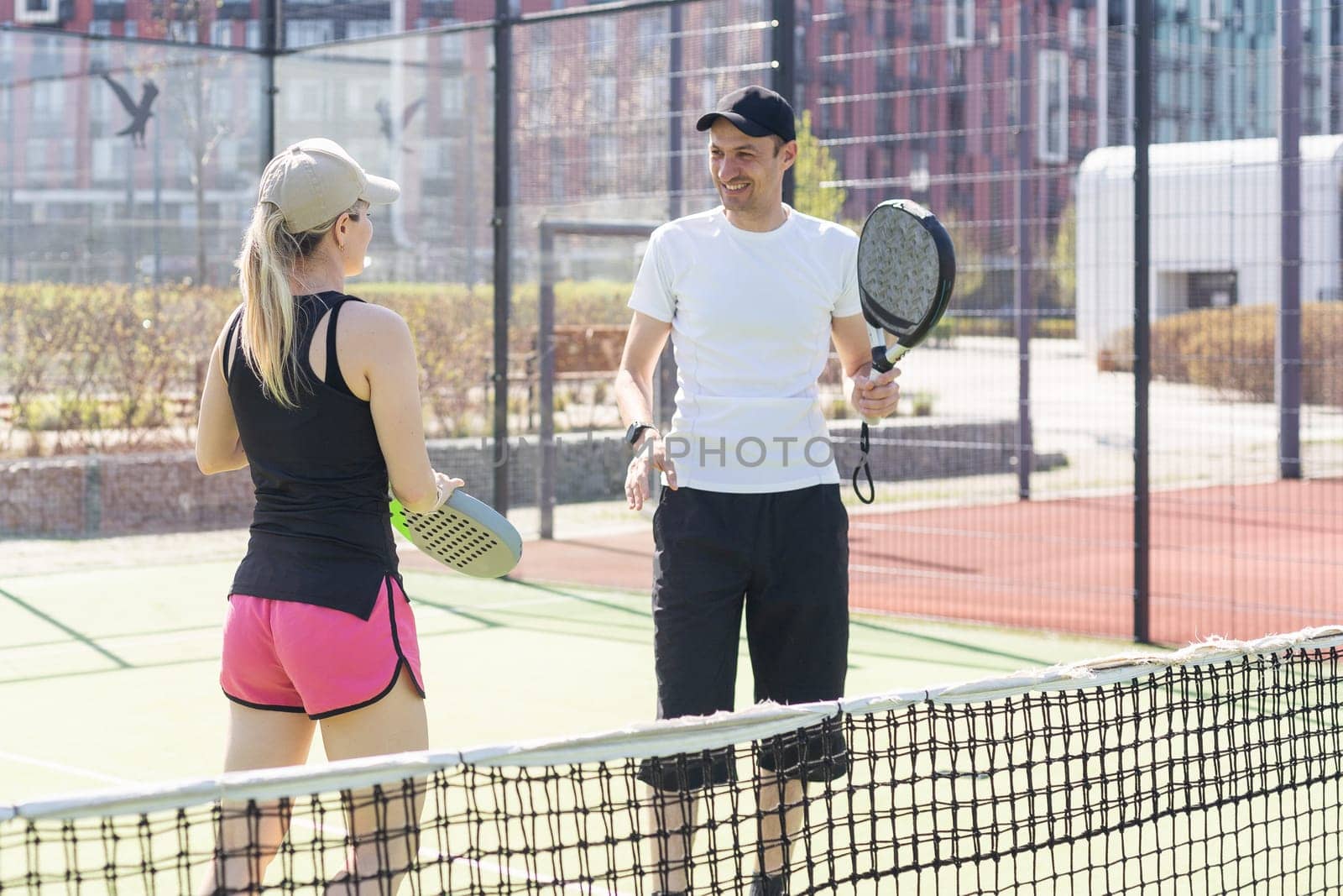 Portrait of positive young woman and adult man standing on padel tennis court, holding racket and ball, smiling. High quality photo