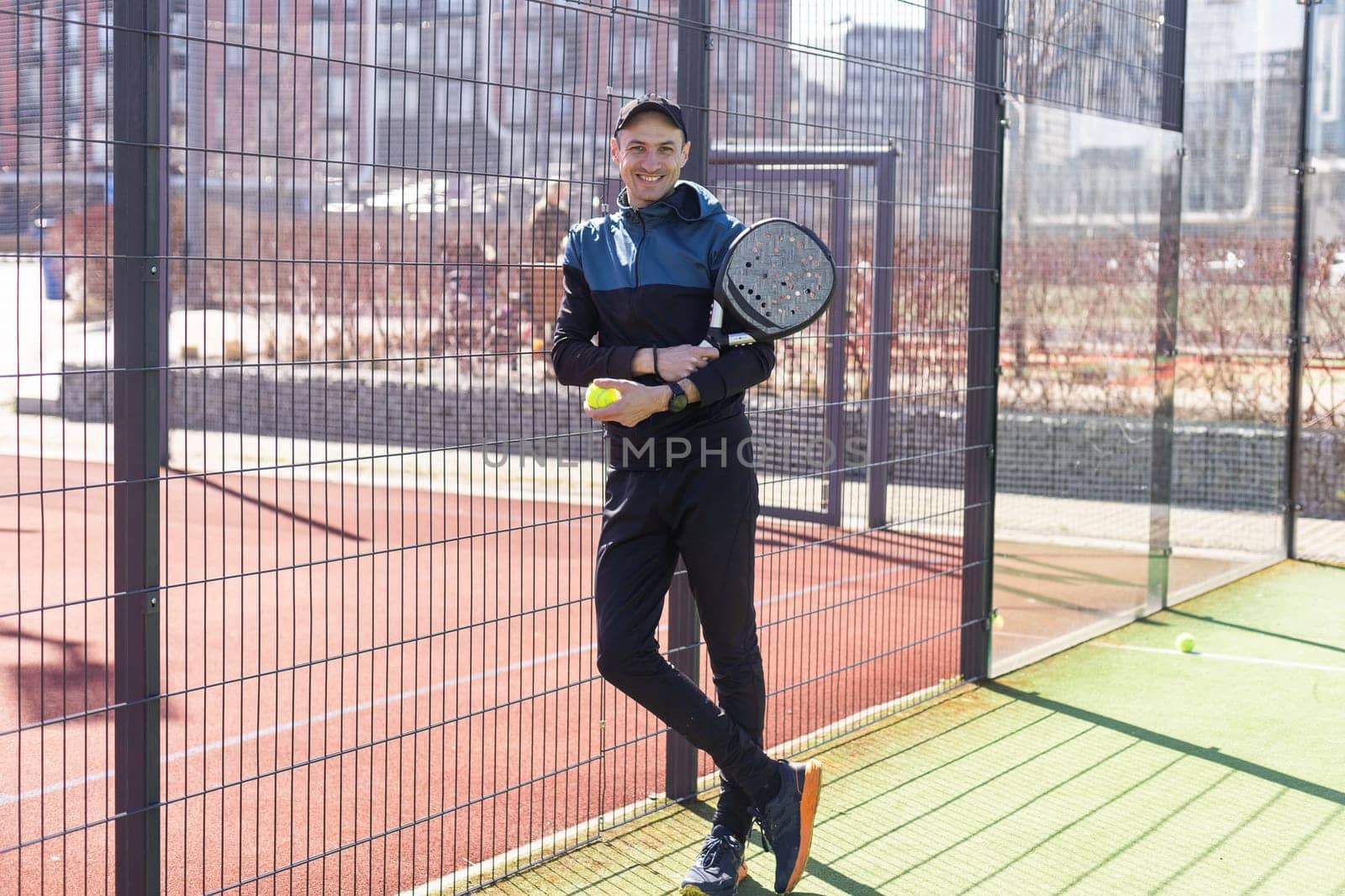 Portrait of positive young man with racket and padel ball on tennis court. High quality photo