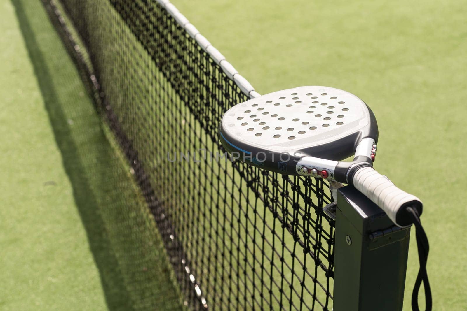 Padel racket and padel ball on a green court in the sunset. High quality photo