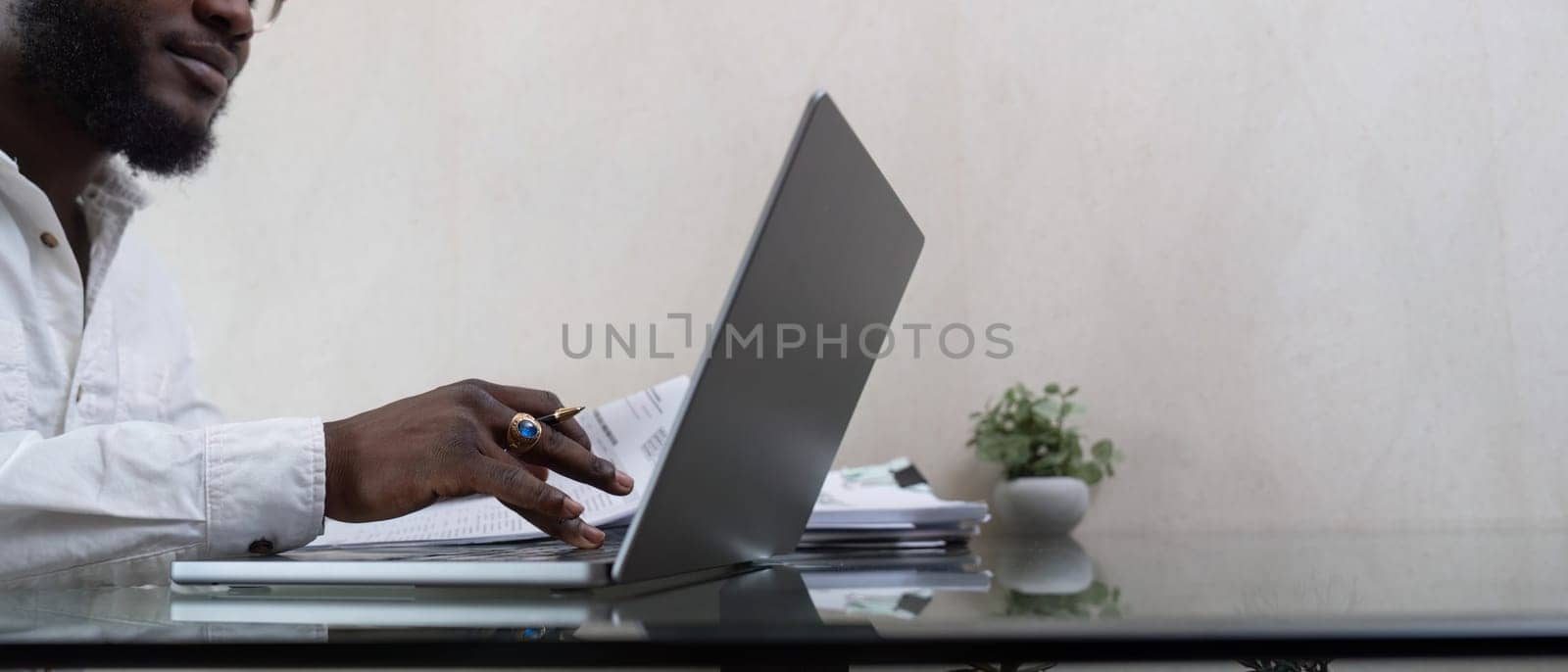 African American man working with laptop computer and using calculator, making financial audit, reviewing bills tax and accounting in living room. Black guy do freelance work at home office by nateemee