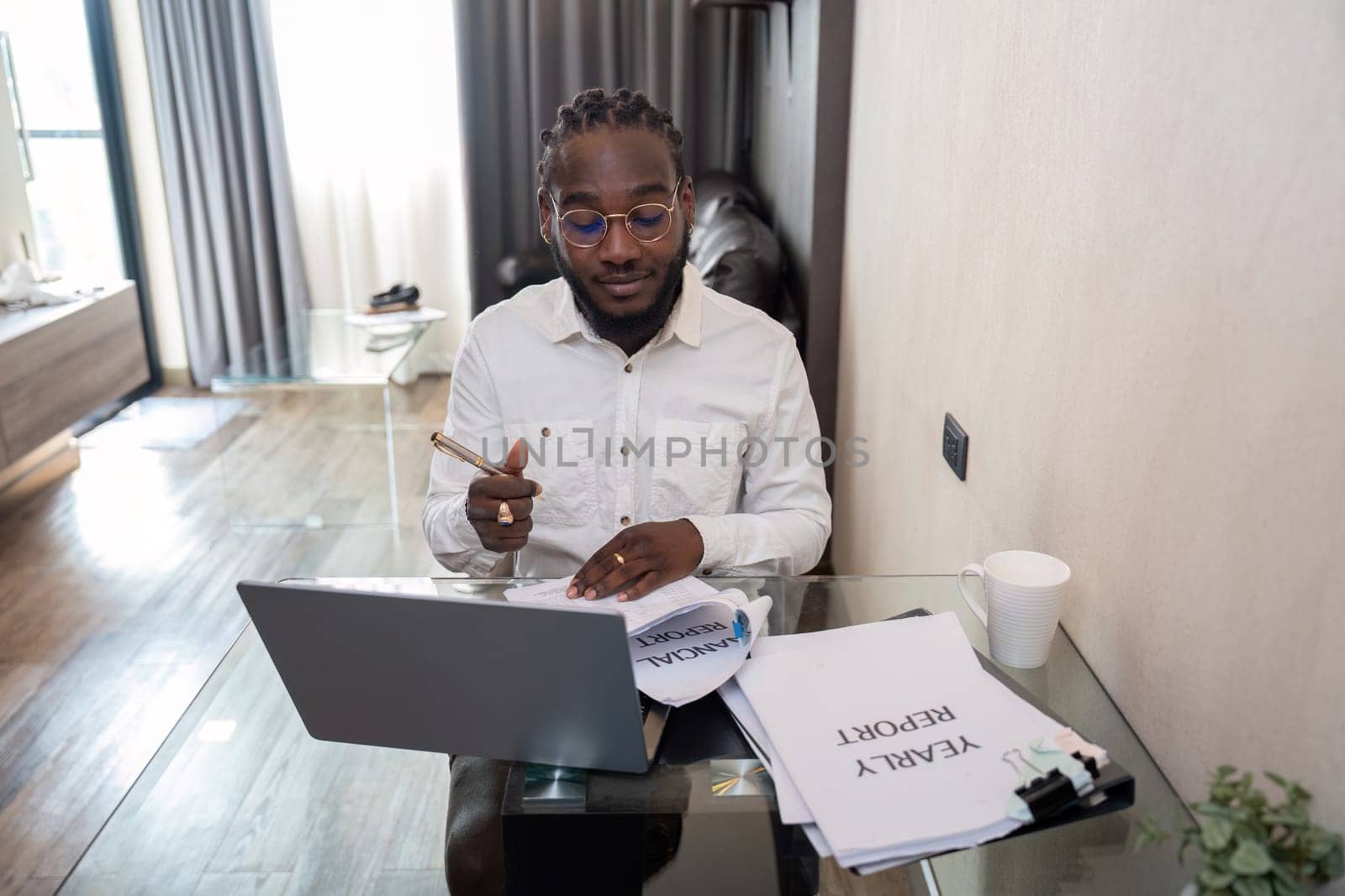 African American man working with laptop computer remote while sitting at glass table in living room. Black guy do freelance work at home office.