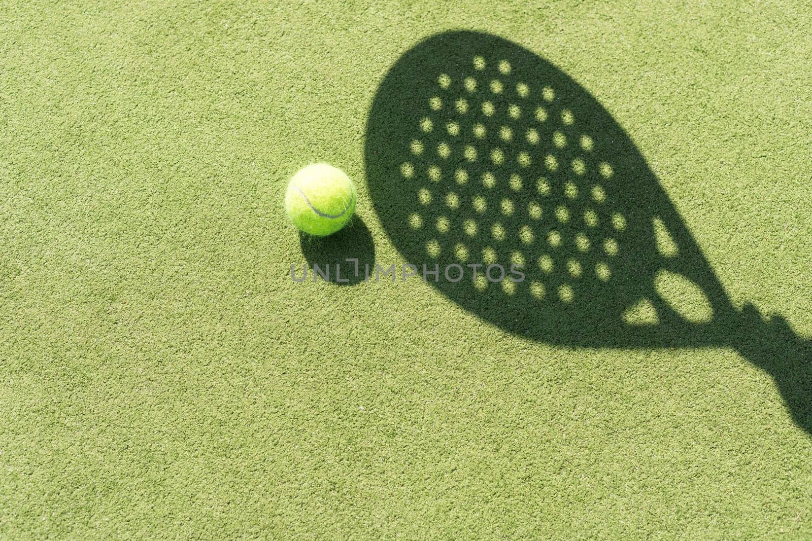 Shadow of a padel racket with a yellow ball on the green grass. High quality photo