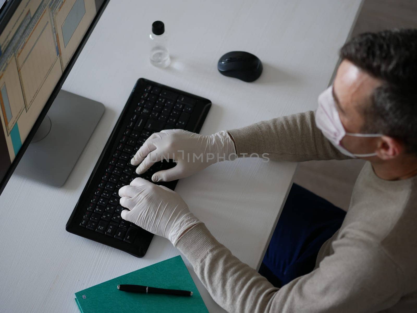Young woman wearing protective gloves on hands and mask on face working from office or home using laptop on desk. by Jyliana
