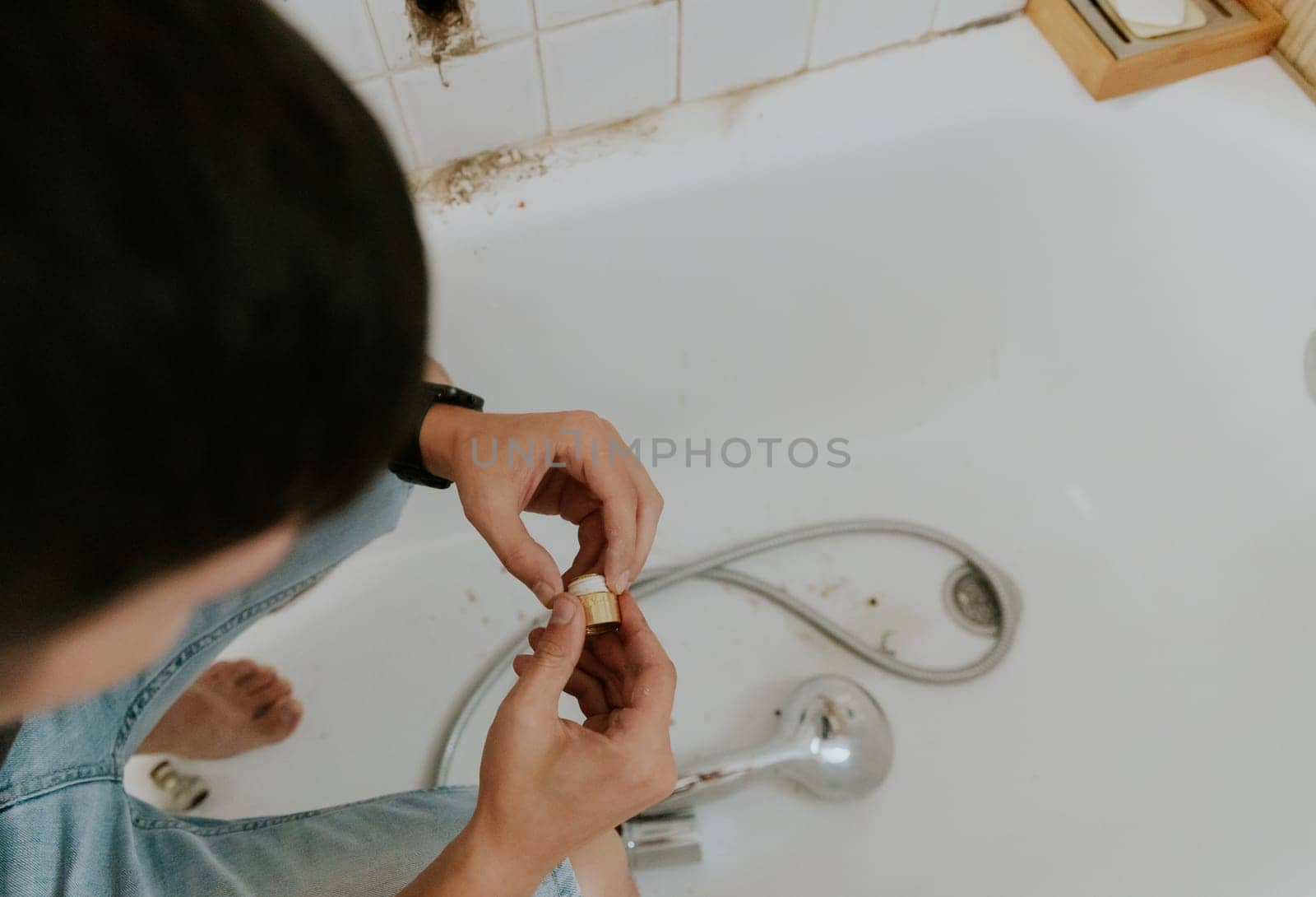 One young Caucasian recognizable guy with a brunette wraps white tow on the nut from the faucet while sitting right in the bathroom at home, close-up side view.Step by step.