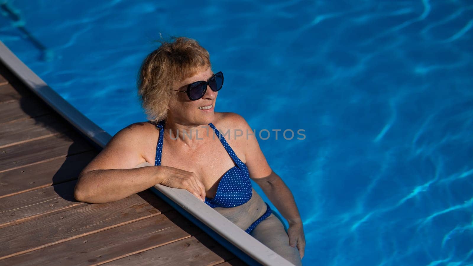 An elderly woman in sunglasses swims in the pool. Vacation in retirement