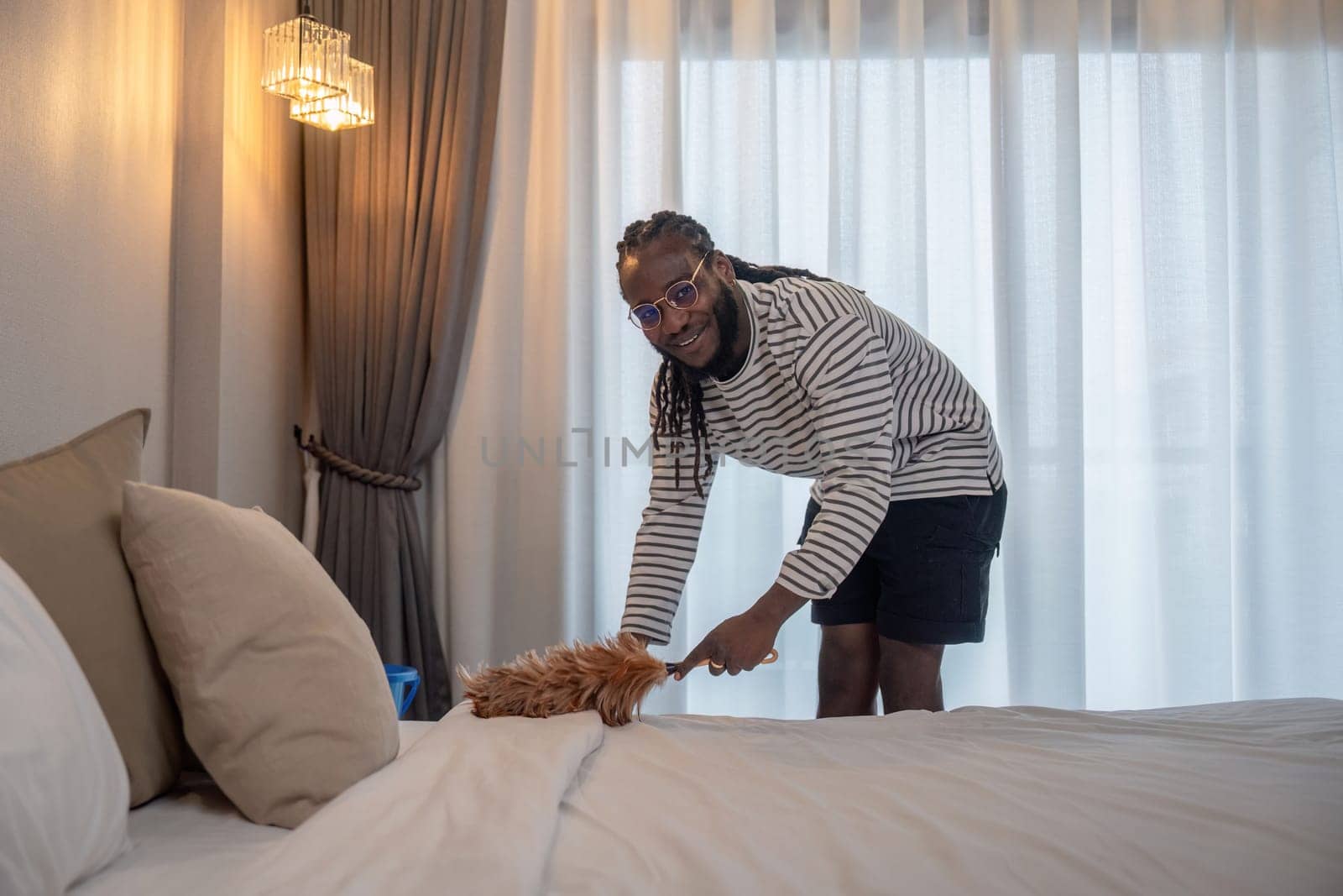 Happy young African American man clean and mop the bed at home.