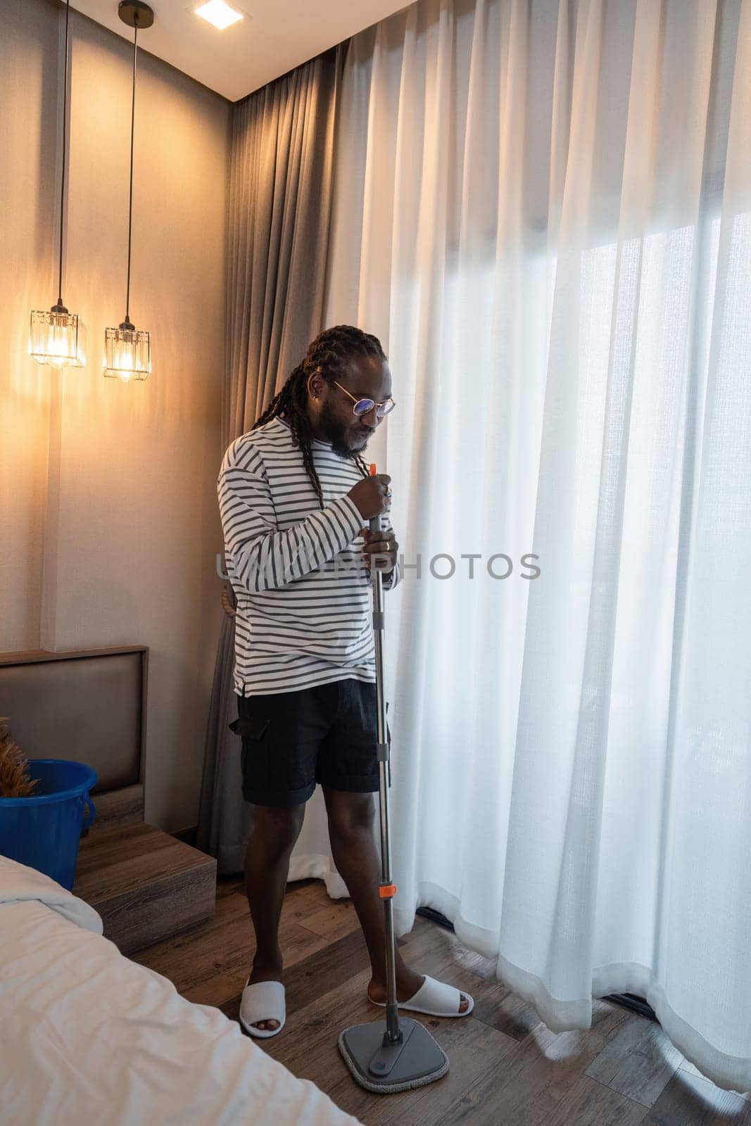 African American man young wipe the floor with a mop while singing in the room at home.