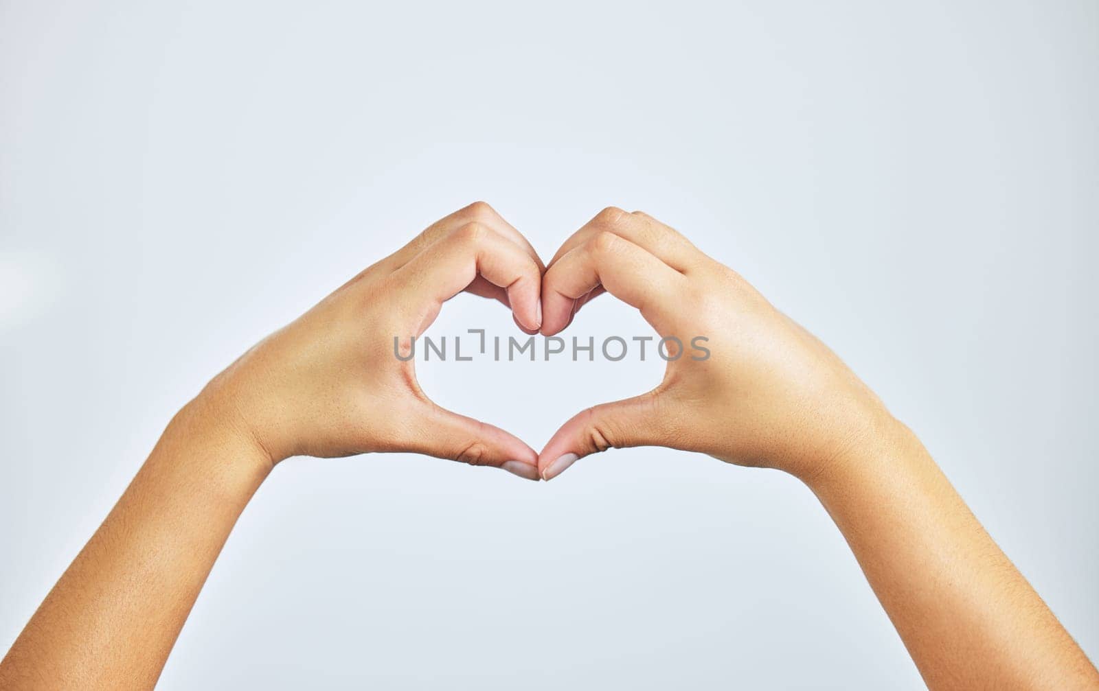 Hands, closeup and person in studio with heart sign, gesture or symbol isolated on white background. Zoom, love and care icon with romance emoji for compassion, kindness and happiness for valentines by YuriArcurs
