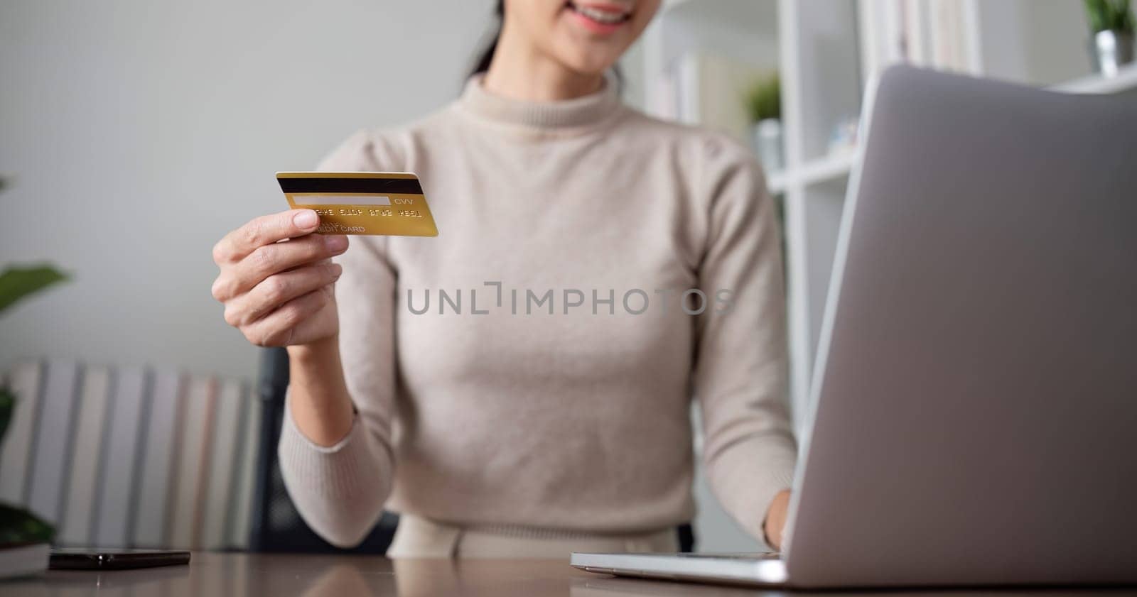 Beautiful young woman uses laptop to shop online, buys things and pays with credit card through phone online banking app..