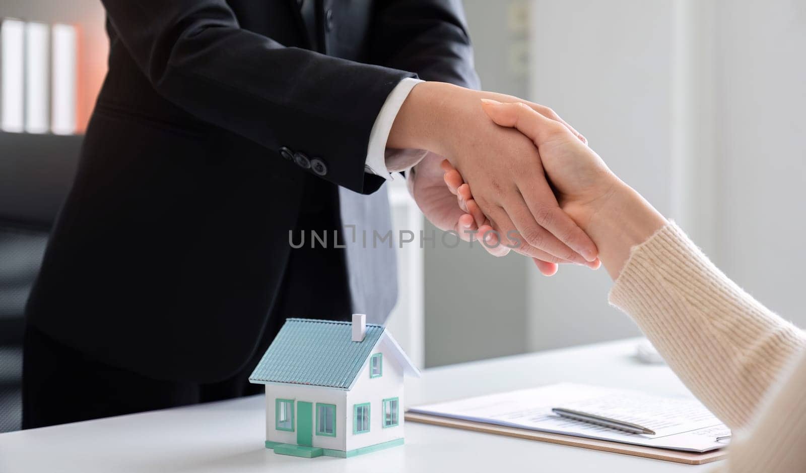 Real estate agent or realtor shakes hands with her client after making the deal in the office.