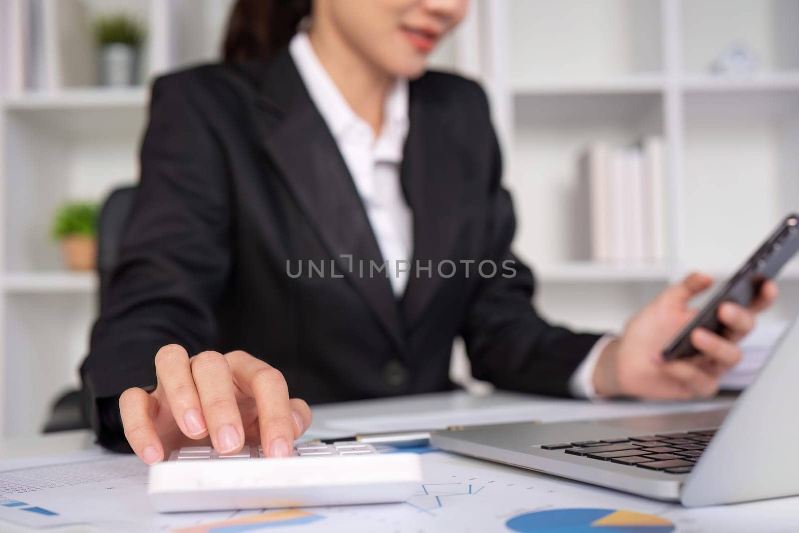 Asian female accountant Use a calculator to calculate business numbers on a white wooden table in the office. by wichayada
