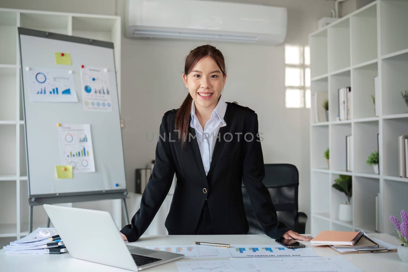 Portrait of a confident young Asian business woman standing at a desk in the office. by wichayada